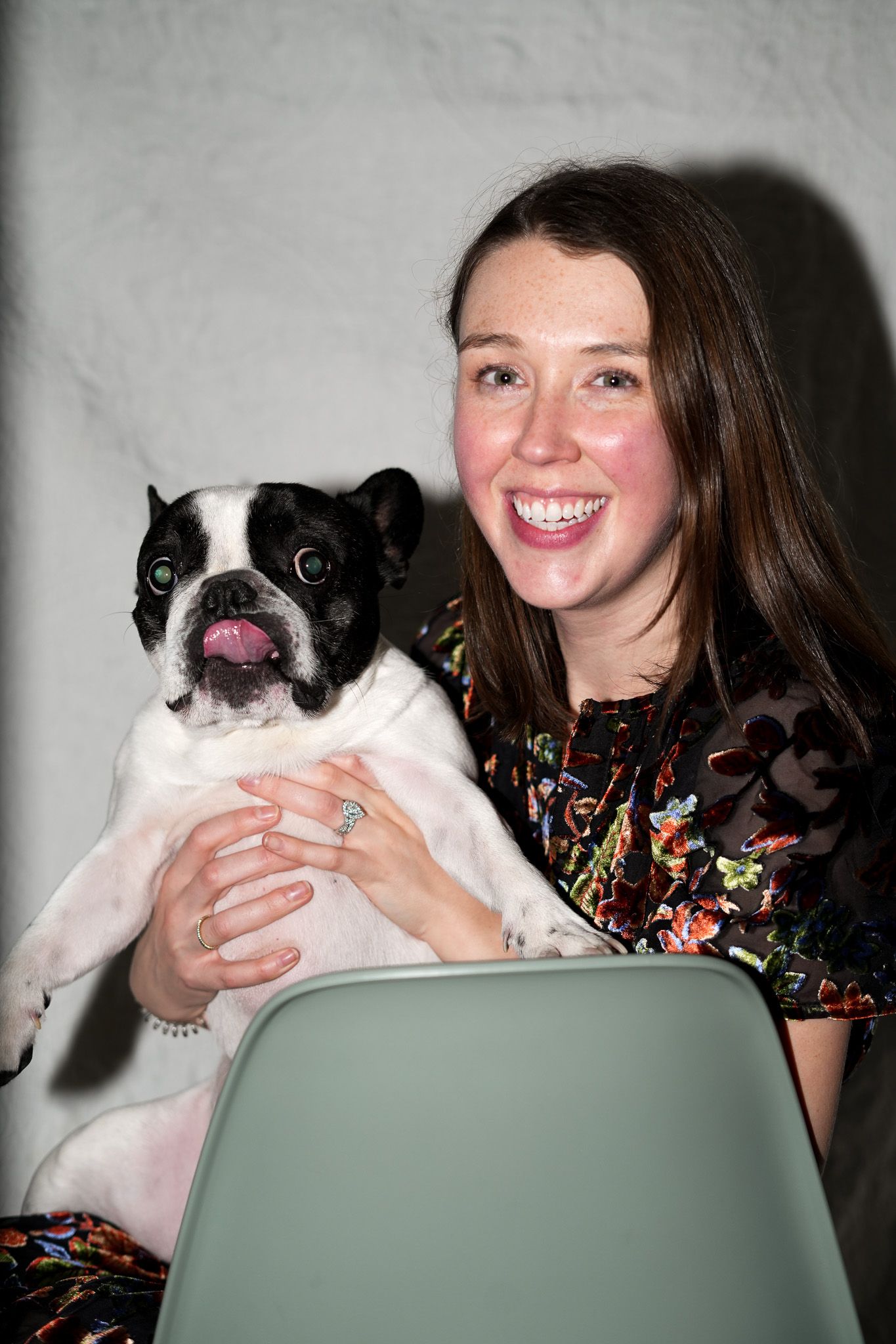 A French Bulldog with black and white markings sits with someone in a floral dress on a gray chair | Sydney Allen Photography