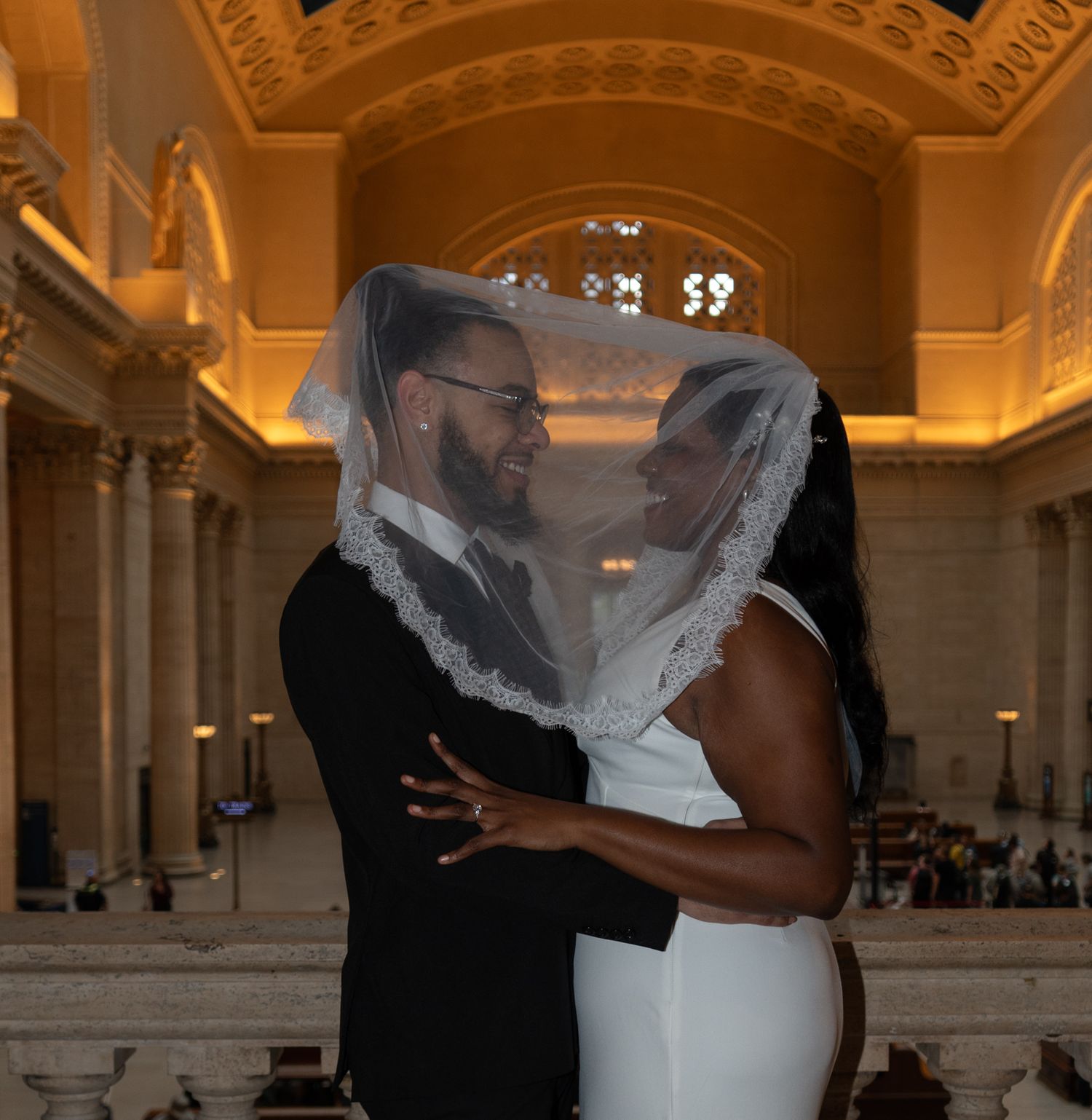 Newlywed couple sharing a romantic moment under a bridal veil in an elegant golden wedding venue.