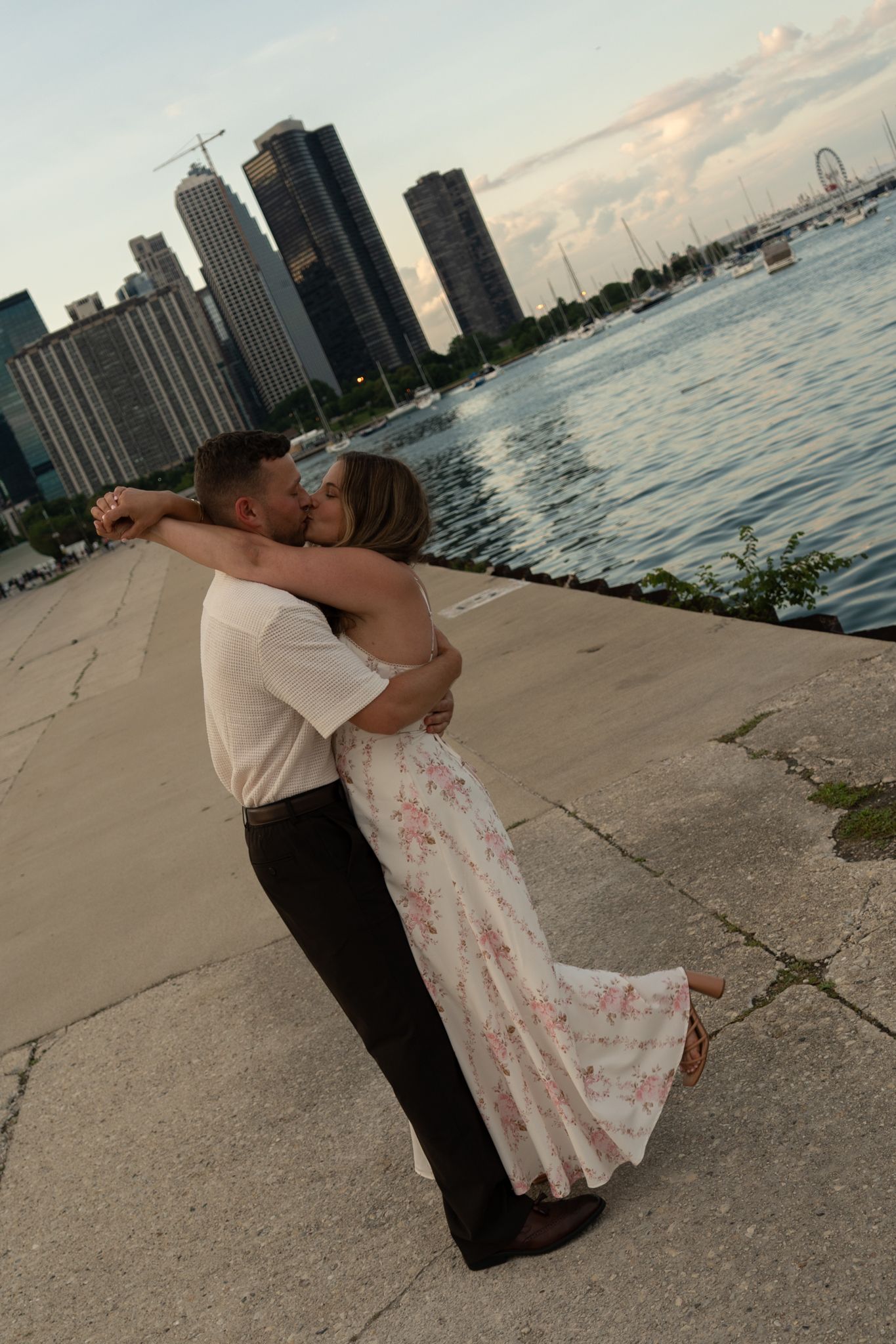Couple sharing a romantic kiss at Chicago waterfront with city skyline and Ferris wheel in the background at sunset.