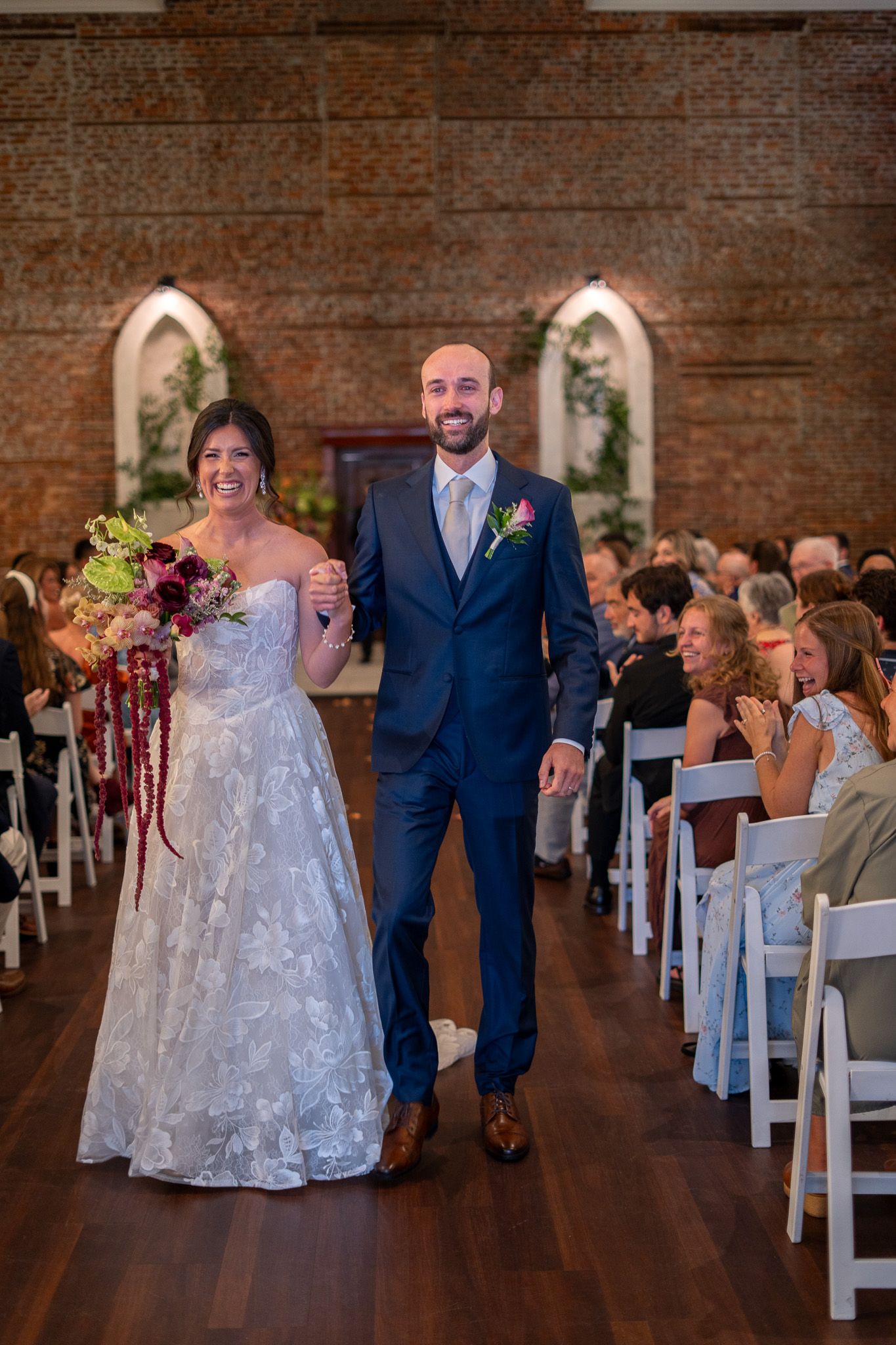 Bride and groom walk joyfully down the aisle after wedding ceremony in a rustic brick venue.