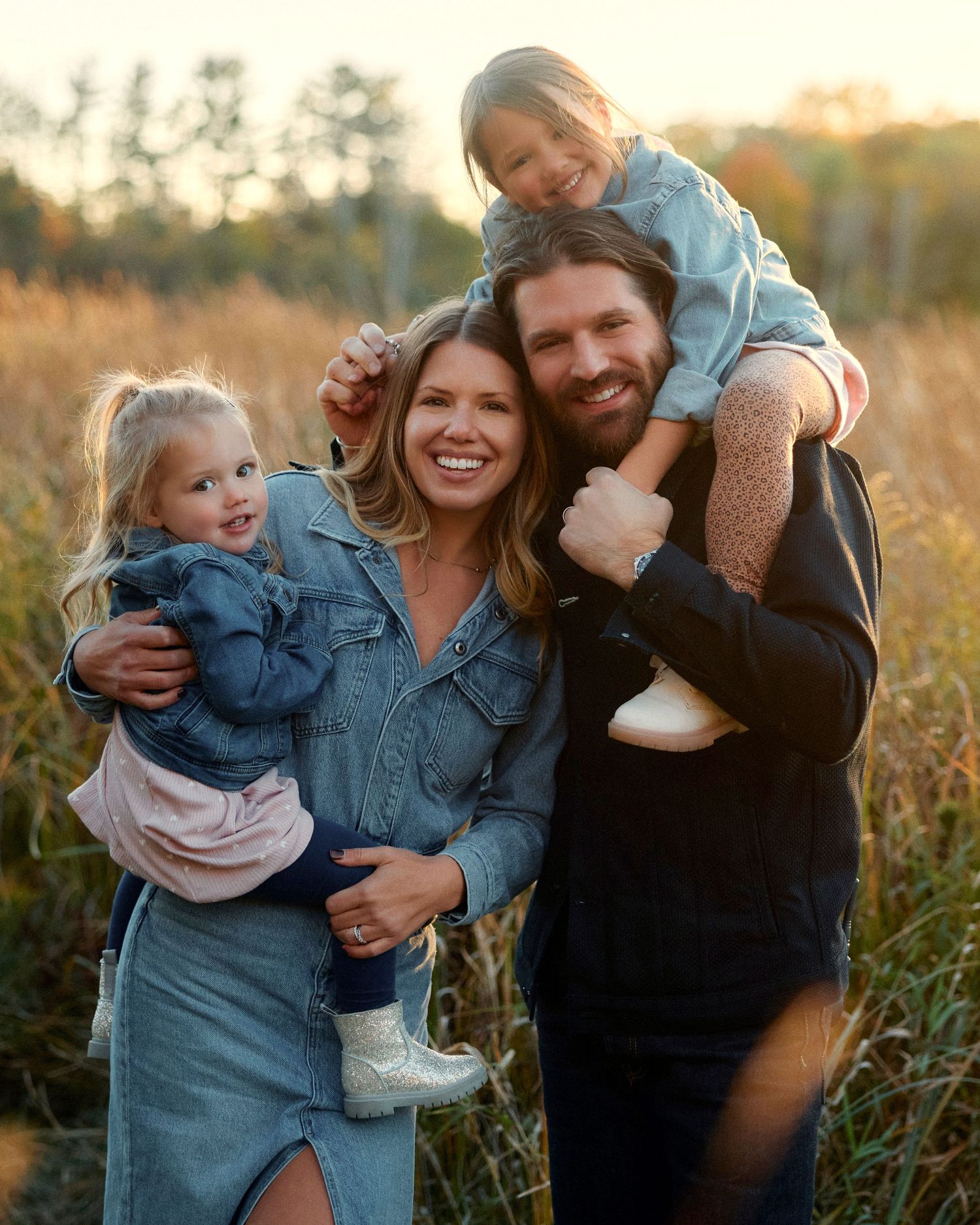 A family shares joyful moments together in a golden sunlit field during sunset.