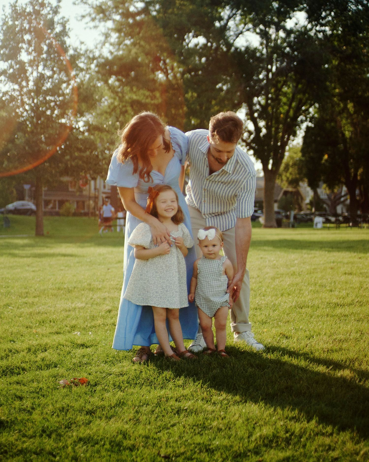 A family group poses together on grass during sunset in a park setting.
