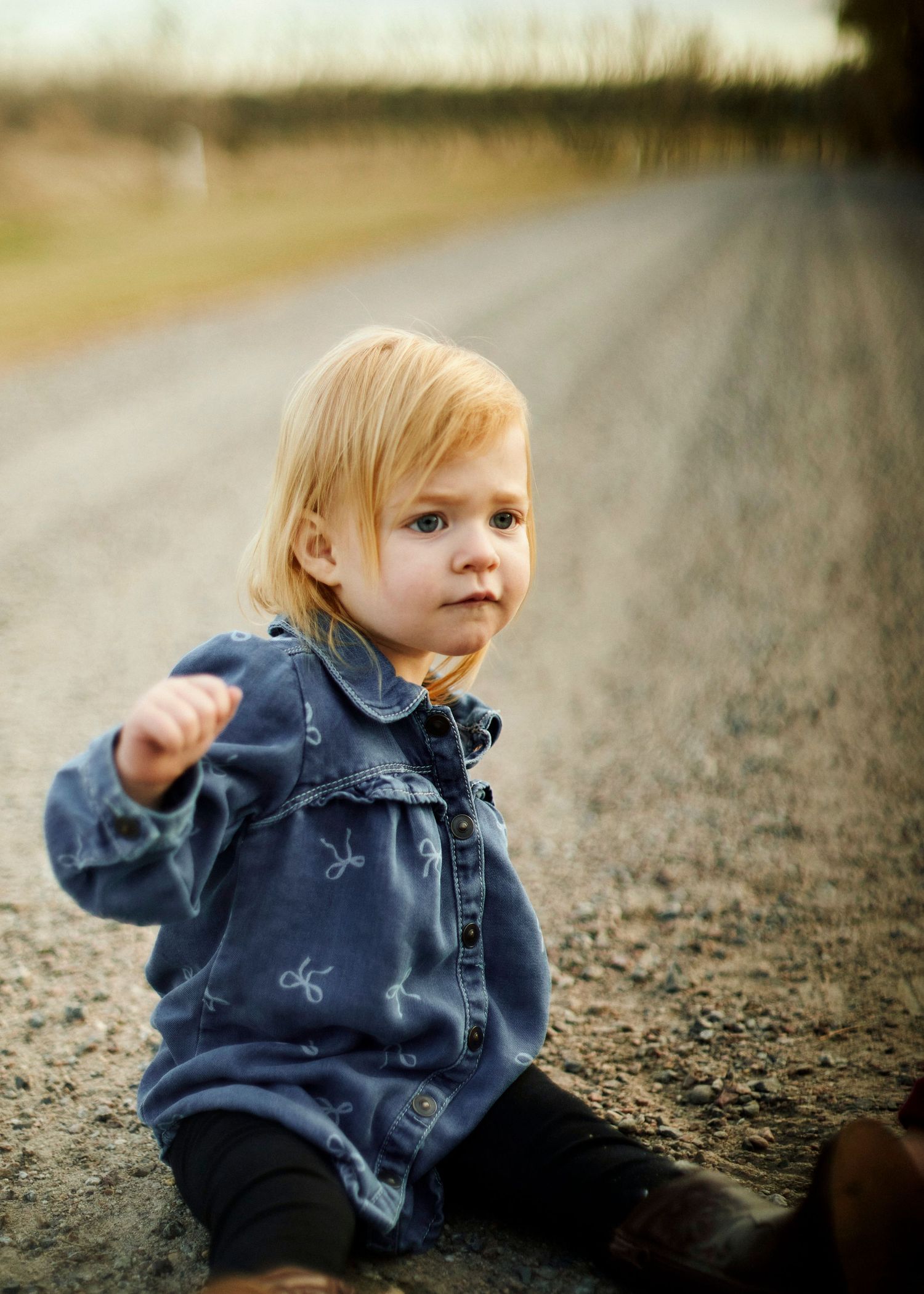 Young child wearing denim jacket sitting on ground during golden hour photoshoot.