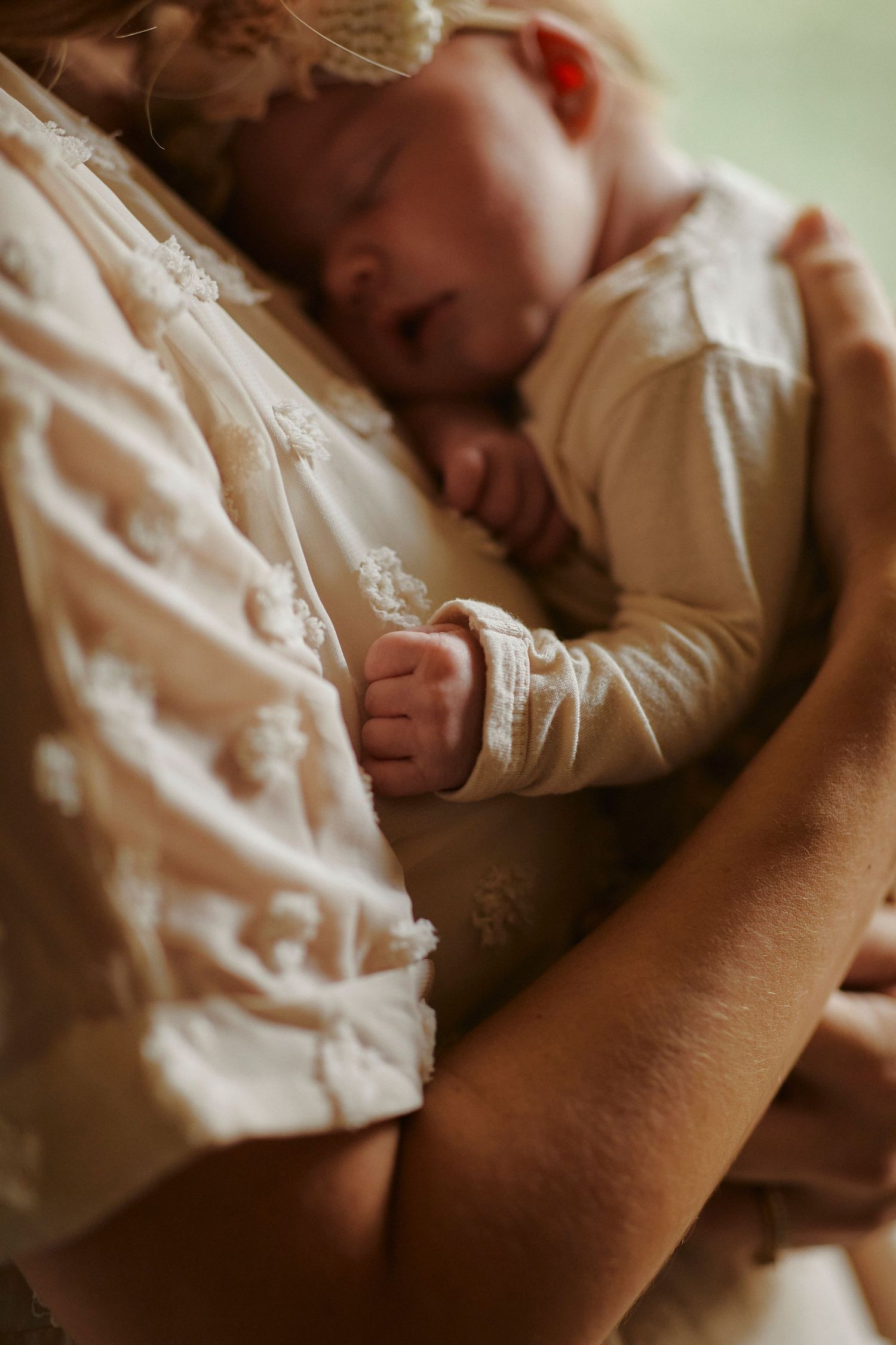 Close-up of a sleeping newborn in white clothing being held against someone's chest.