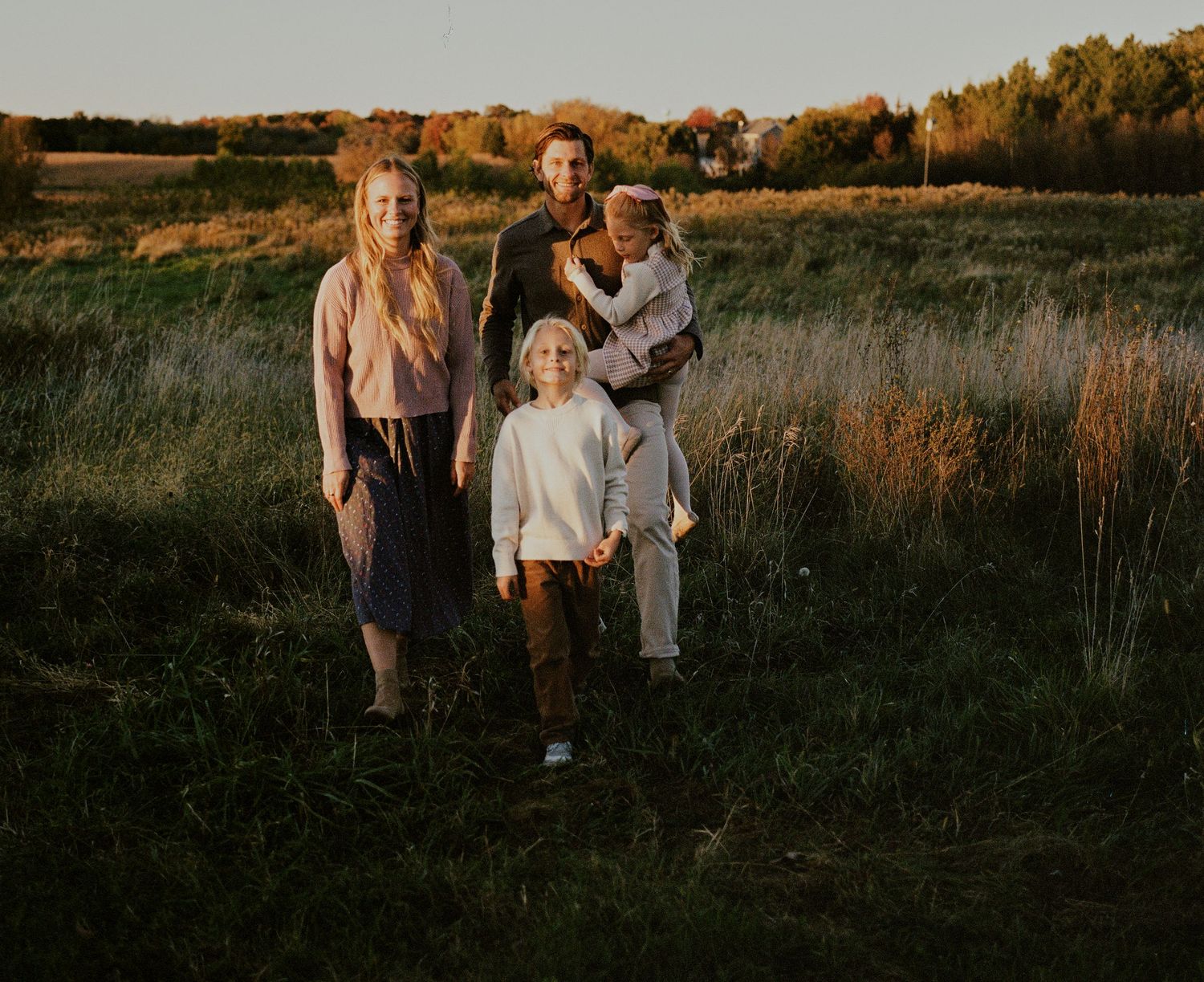 Family walking together through tall grass field during sunset photo session.