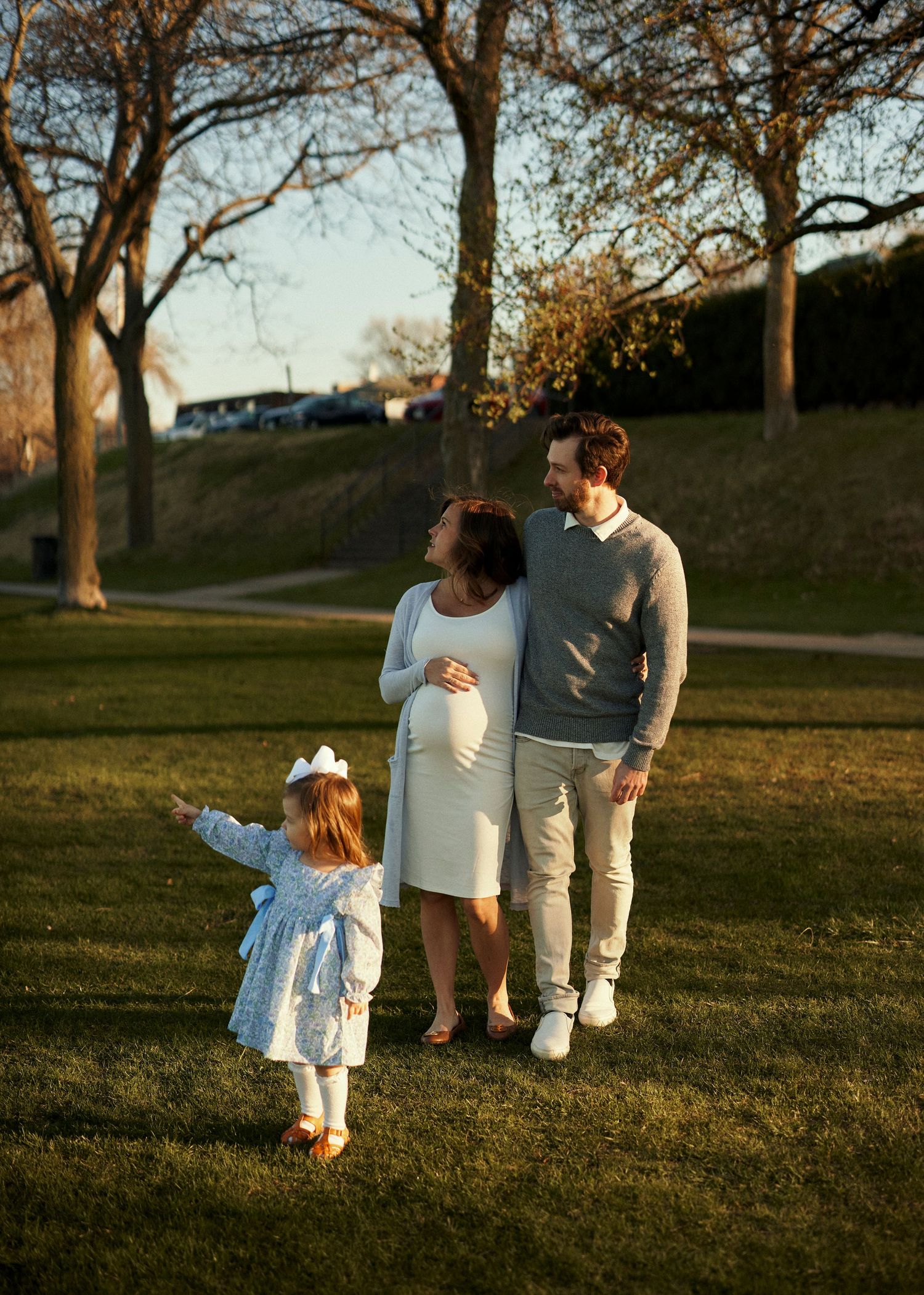 Family walking together in park during sunset with trees in background.