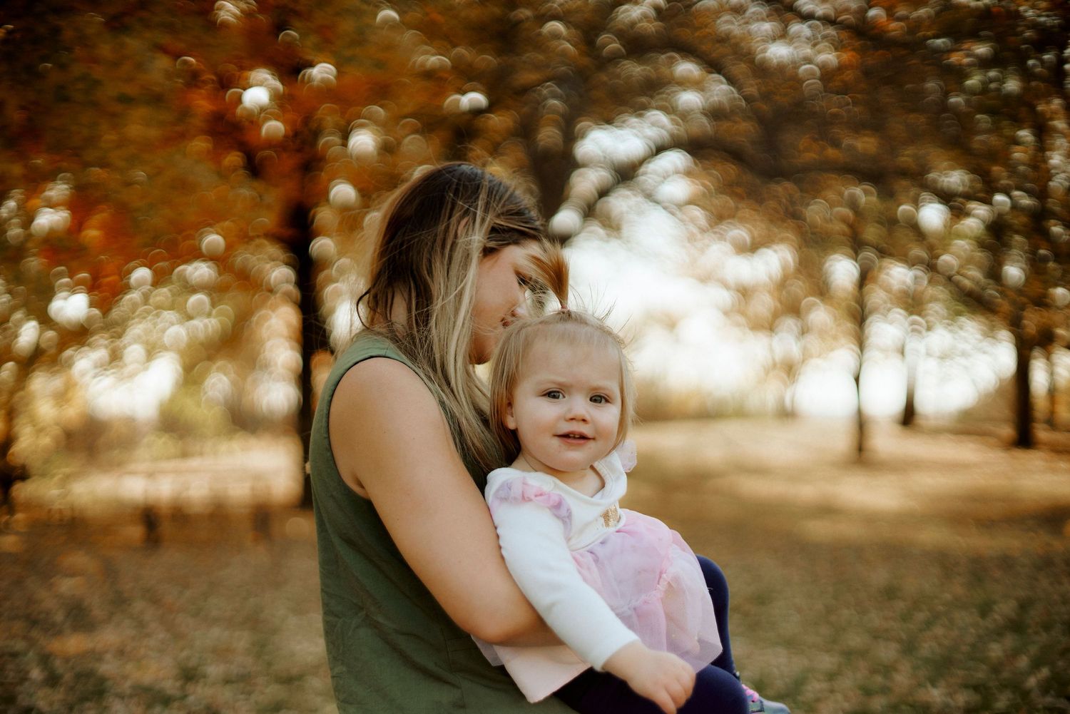 Autumn scene of parent and child embracing under golden trees with bokeh lighting effects.