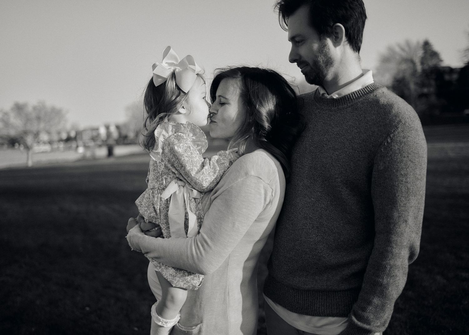 A black and white series of intimate family moments showing parents with a small child in outdoor settings.