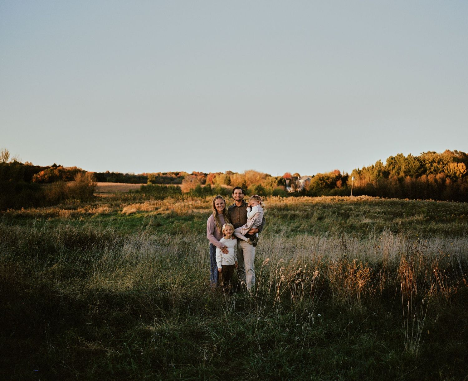 Wide landscape shot of family in field during golden hour photography session.