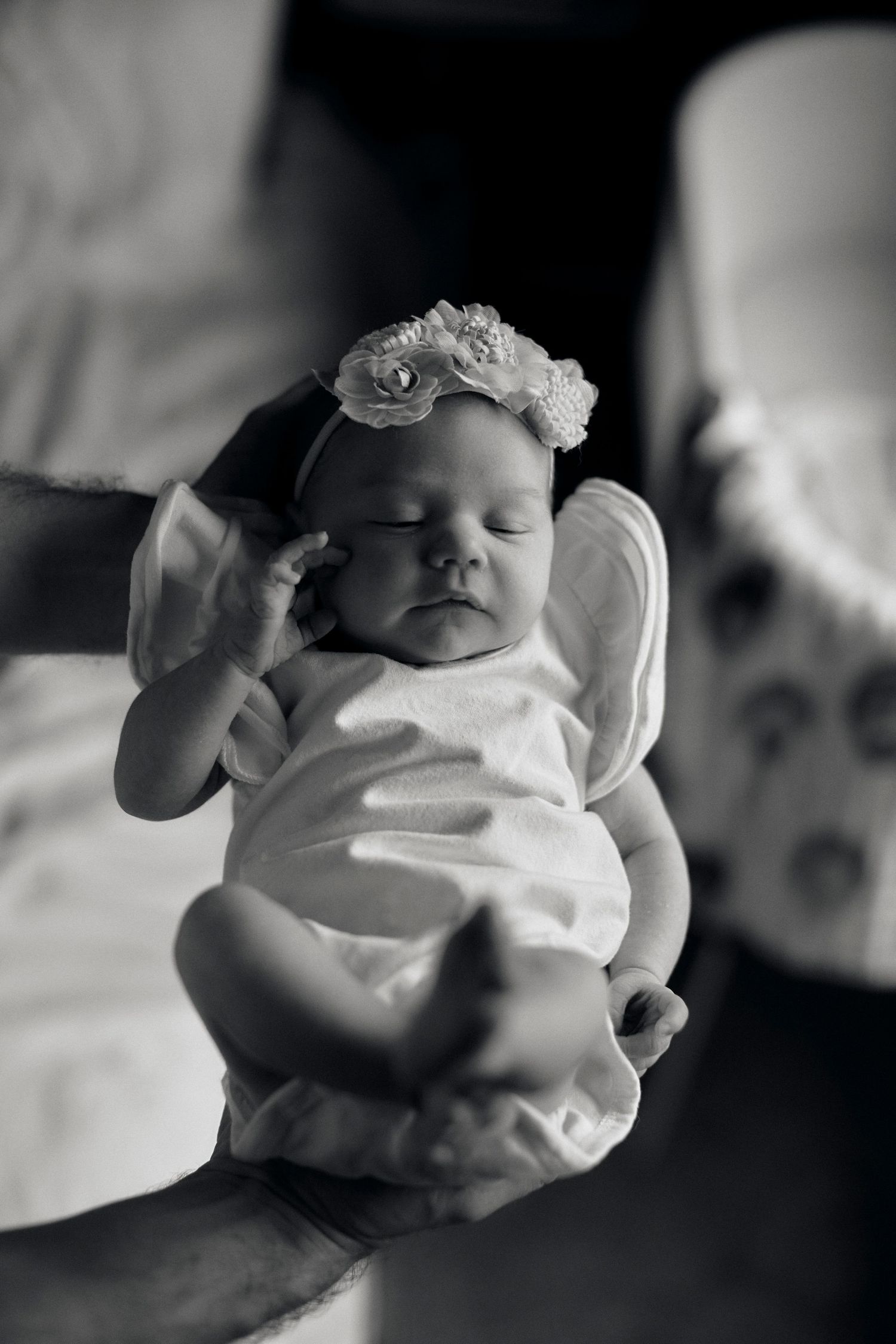 A sleeping newborn baby wearing a delicate lace headband being cradled in black and white.
