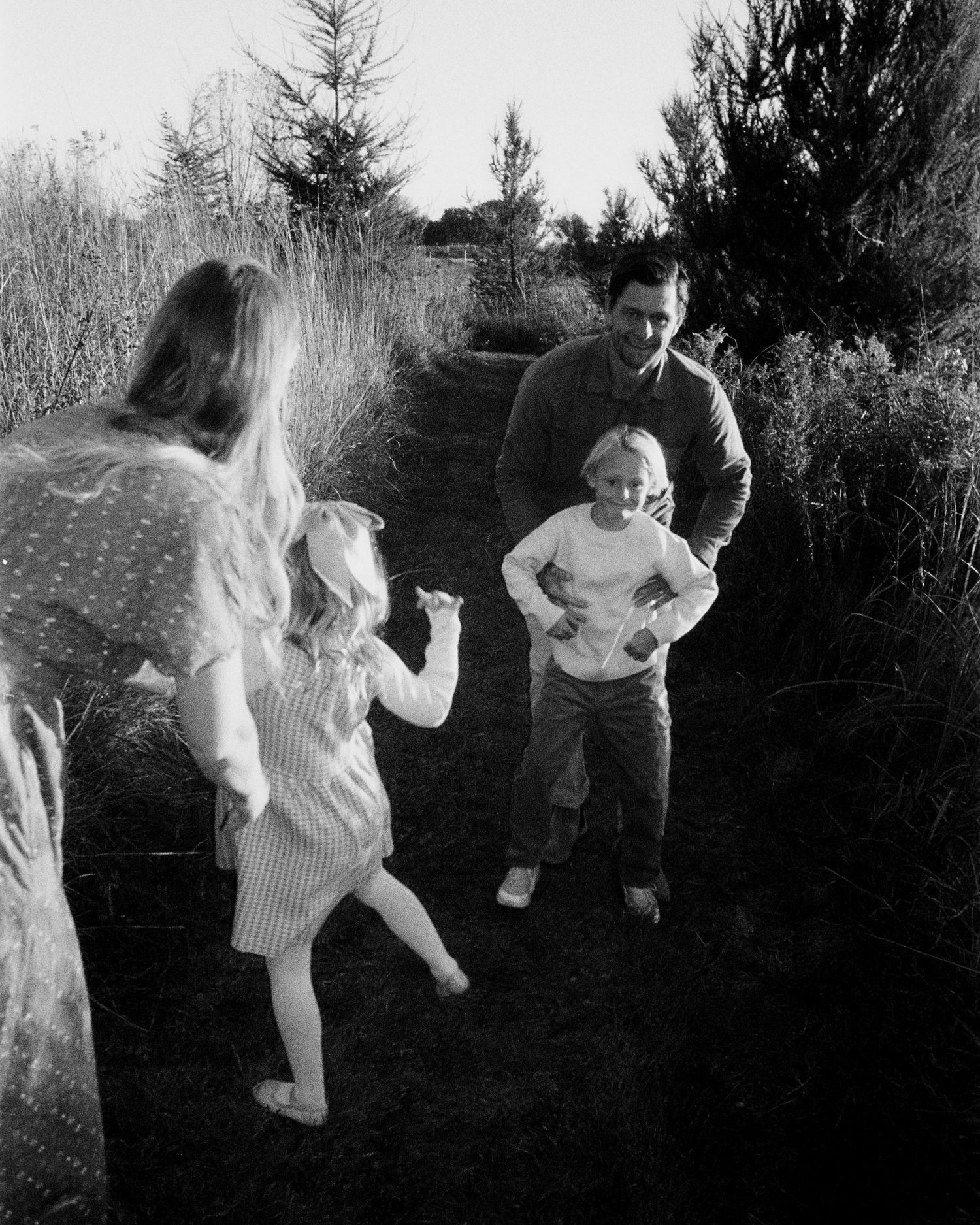 A black and white photo of a family playing together on a garden path surrounded by trees and bushes.