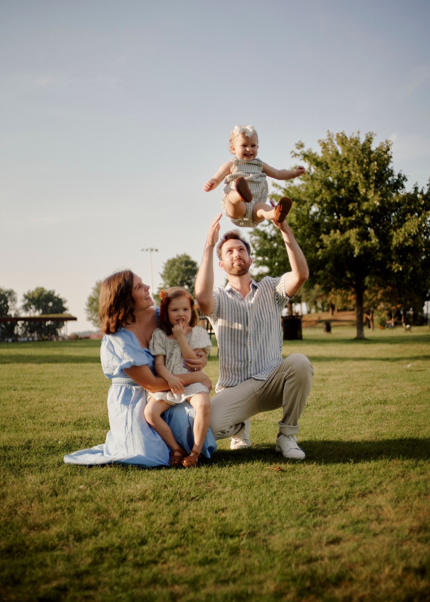 A family enjoys a playful moment together on a grassy hill during golden hour.