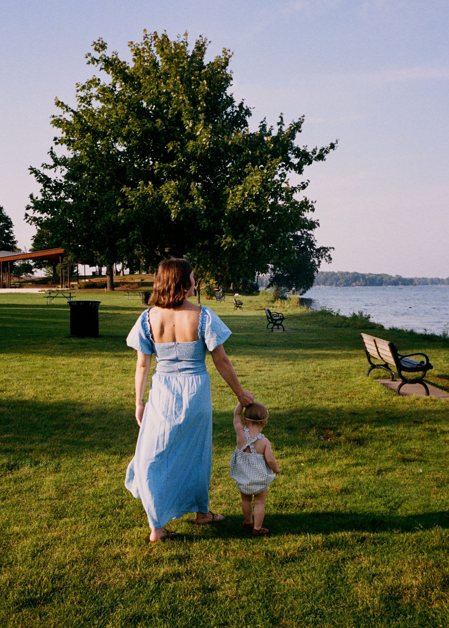 Family walking together on a waterfront lawn during a sunny afternoon.