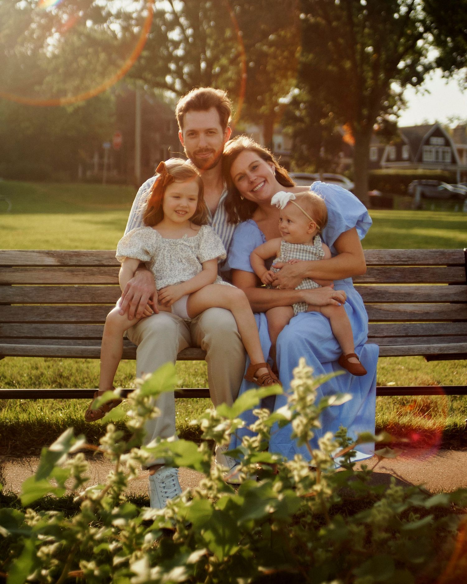 Family relaxing together on a park bench surrounded by blooming flowers at sunset.