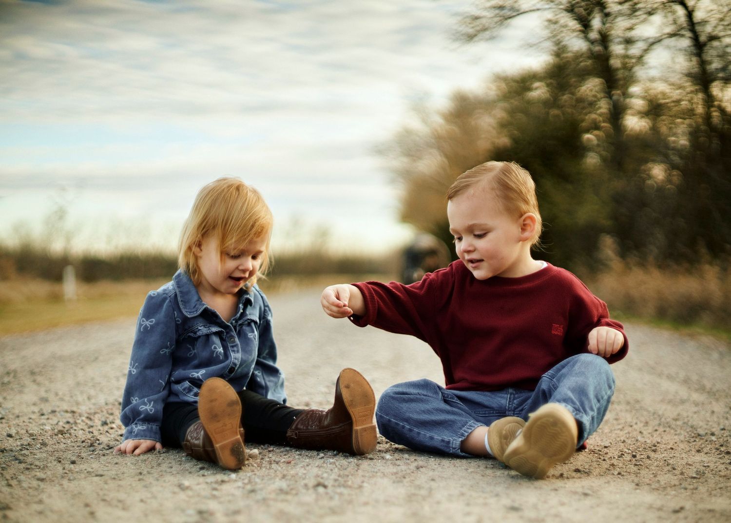 Playful child sitting and crawling on a gravel path during outdoor photoshoot.