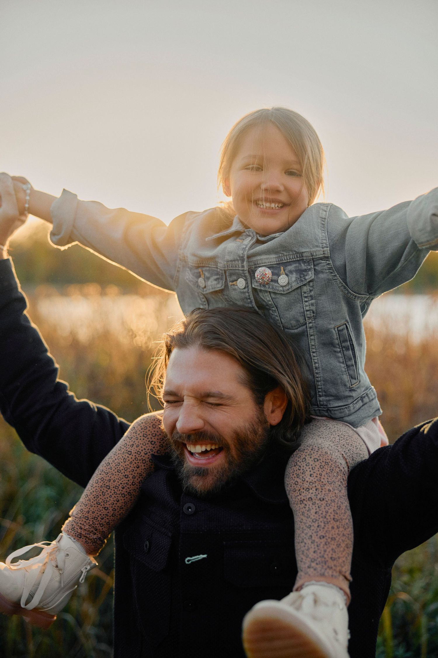 A playful outdoor moment captured at golden hour with a child riding on shoulders during sunset.