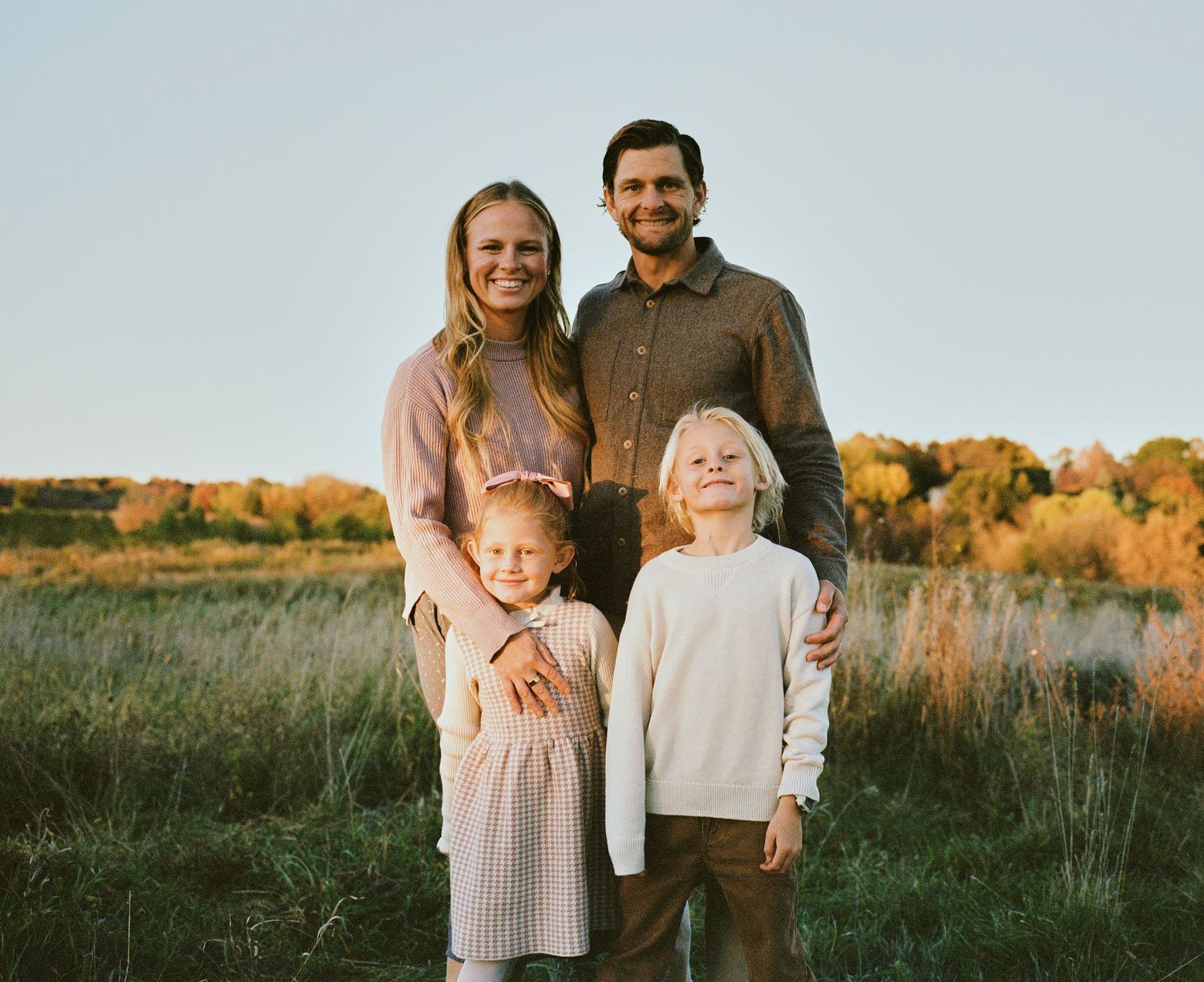 Family portrait in casual attire against autumn landscape at golden hour.