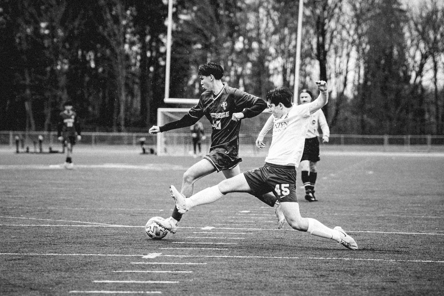 Two soccer players compete for the ball on a grass field in a black and white photograph.