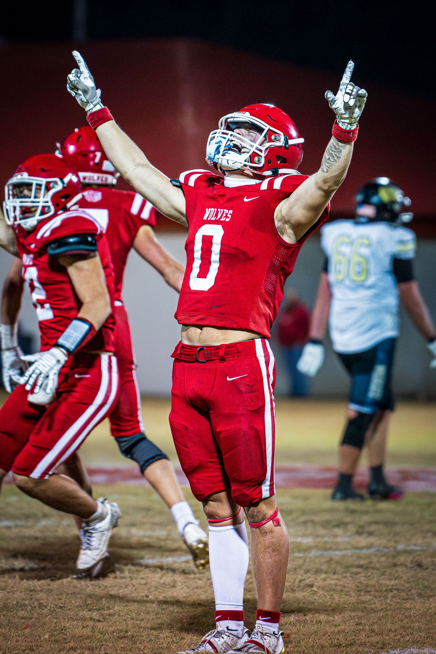 A football player in a red jersey celebrating with his arms raised on the field.