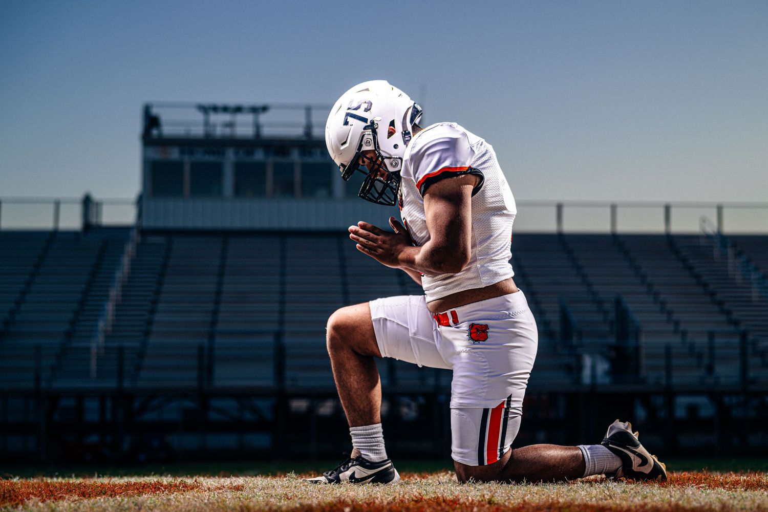 A football player kneeling on the field in a stadium.