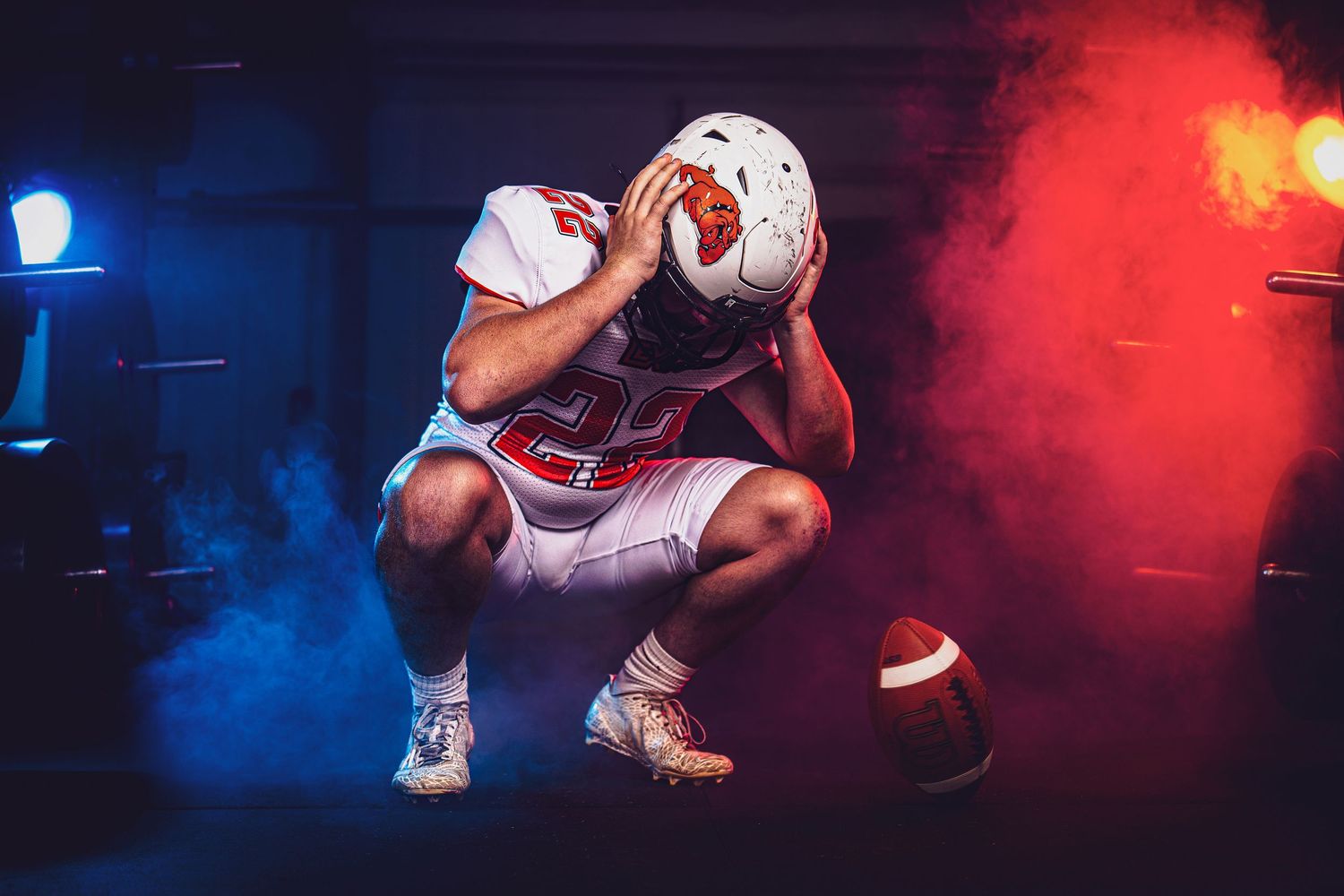 A person wearing a football uniform is crouched on the field amidst smoke and lighting effects.