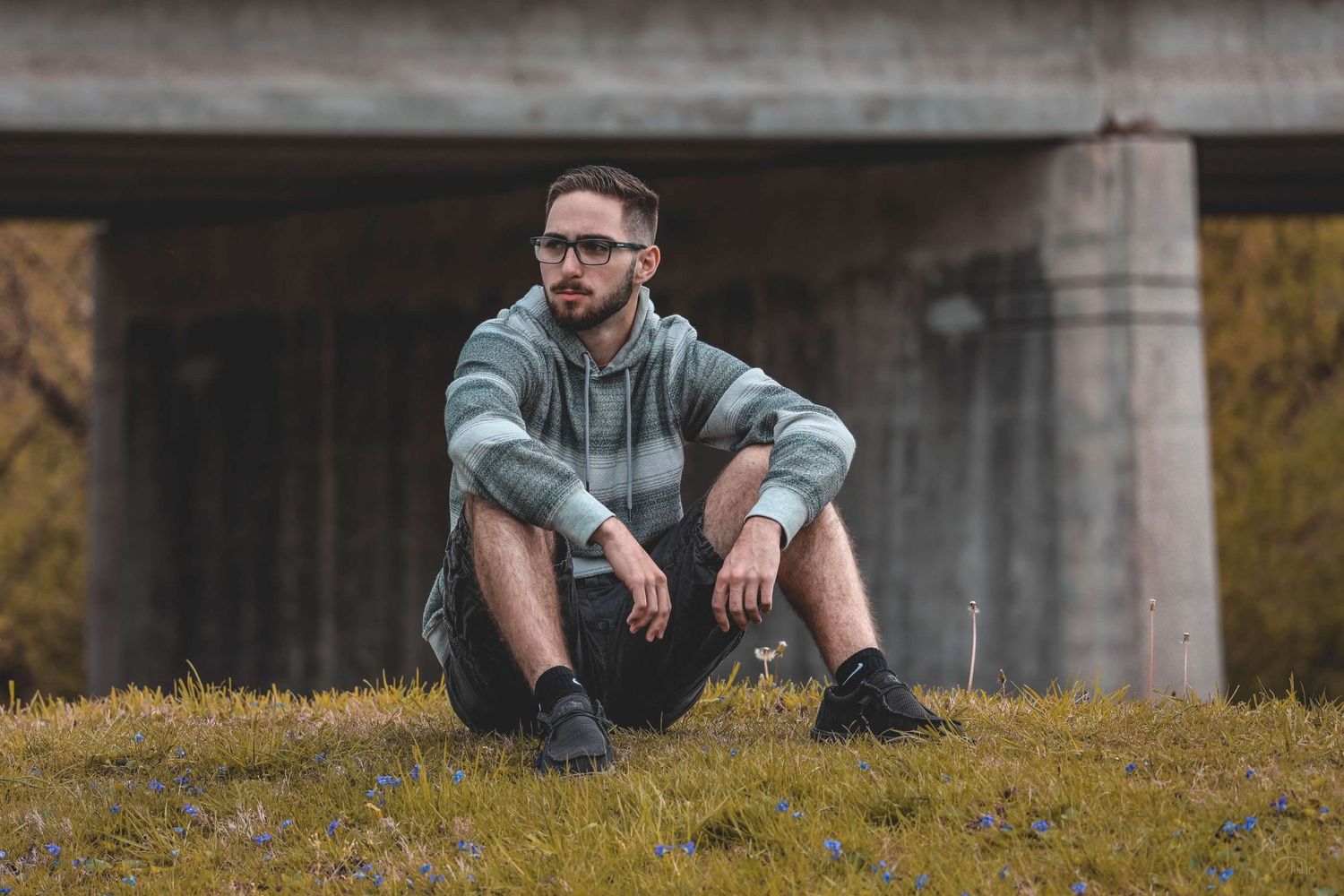 Person sitting casually on grassy slope near concrete structure at sunset.
