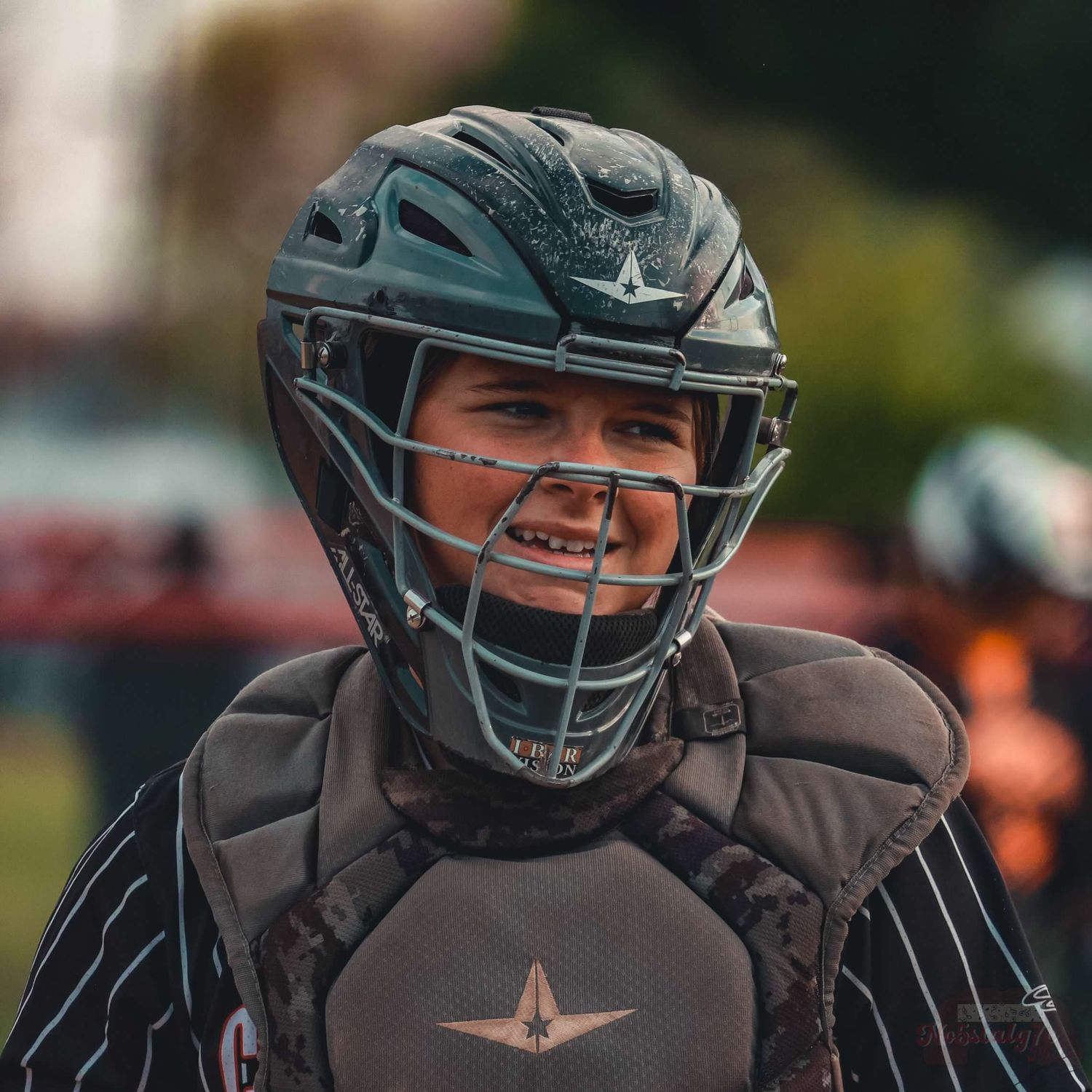 Youth baseball catcher wearing protective gear and helmet smiling during a game.