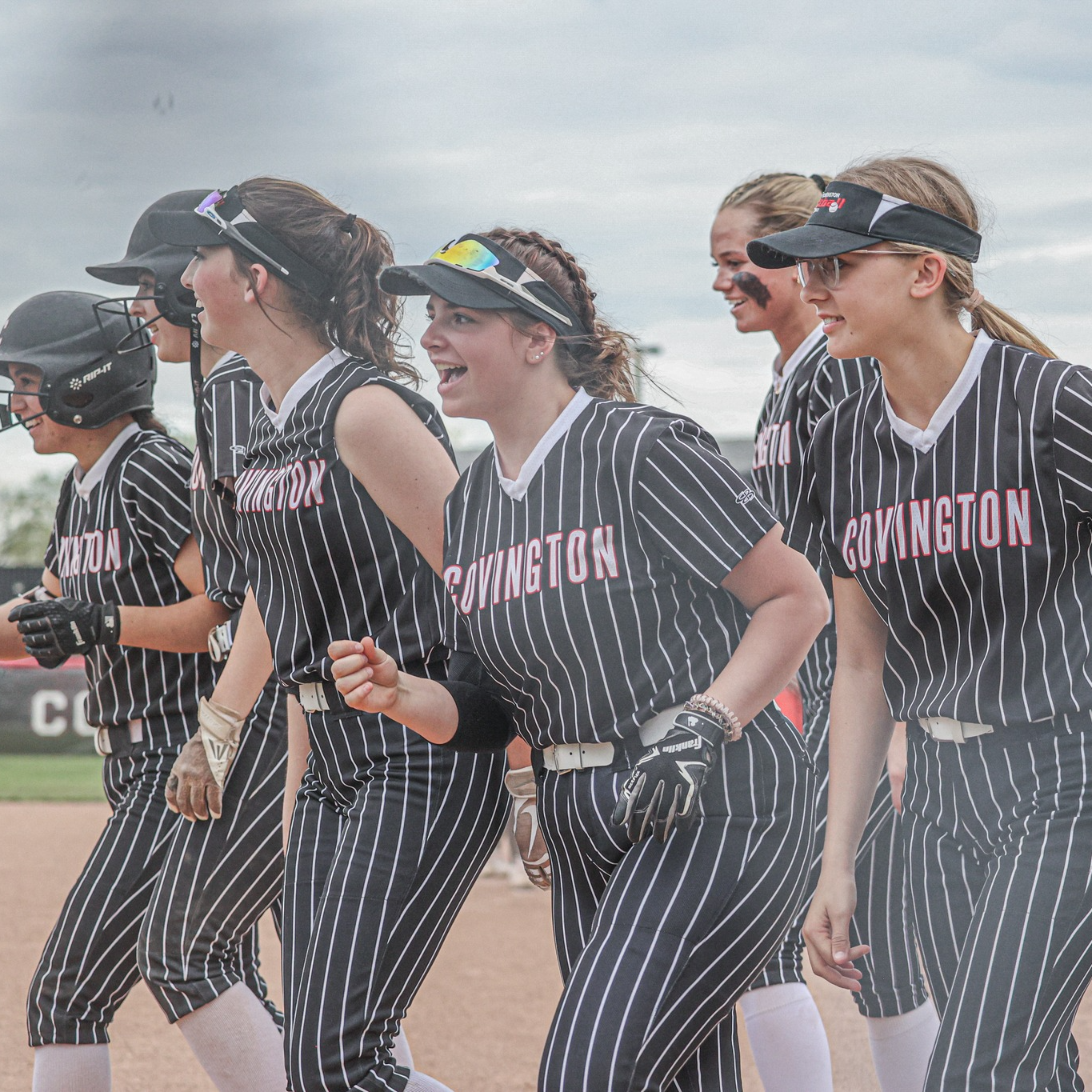 Softball team in pinstriped uniforms walking together on field.