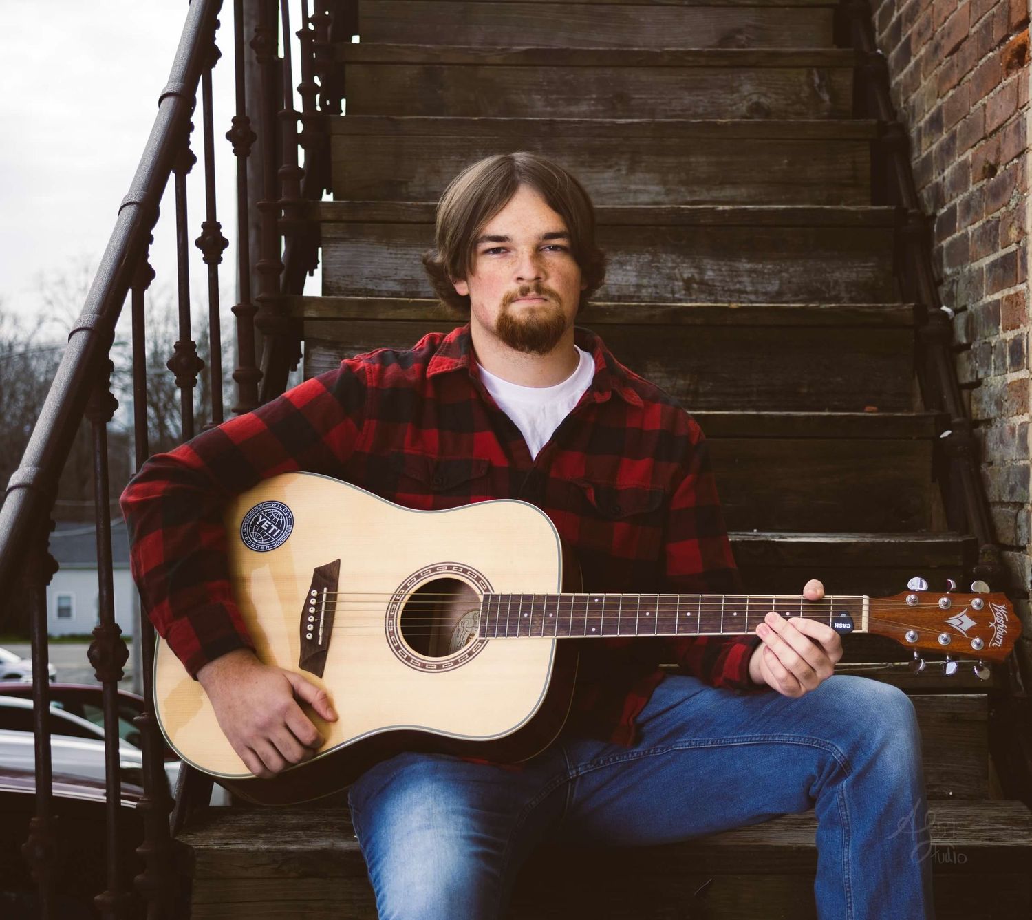 Person sitting on wooden steps playing acoustic guitar in casual attire.