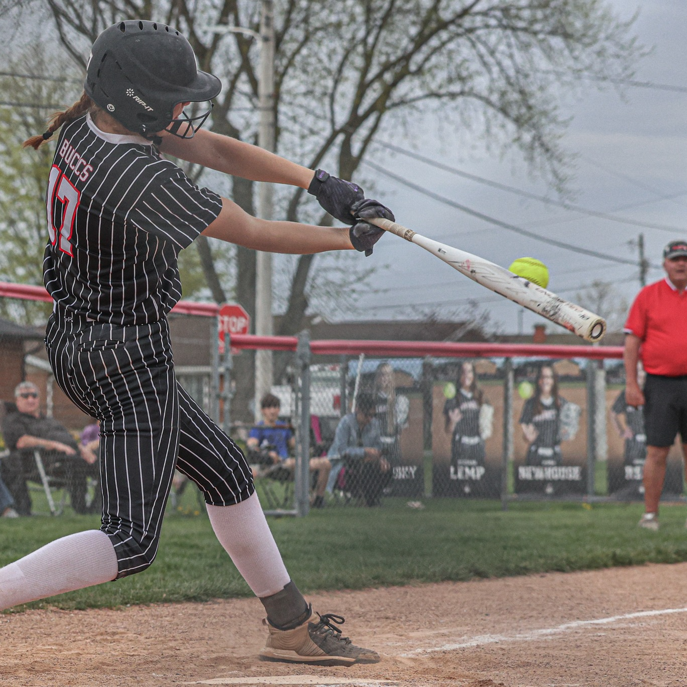 Softball player in pinstripe uniform swings bat during game.
