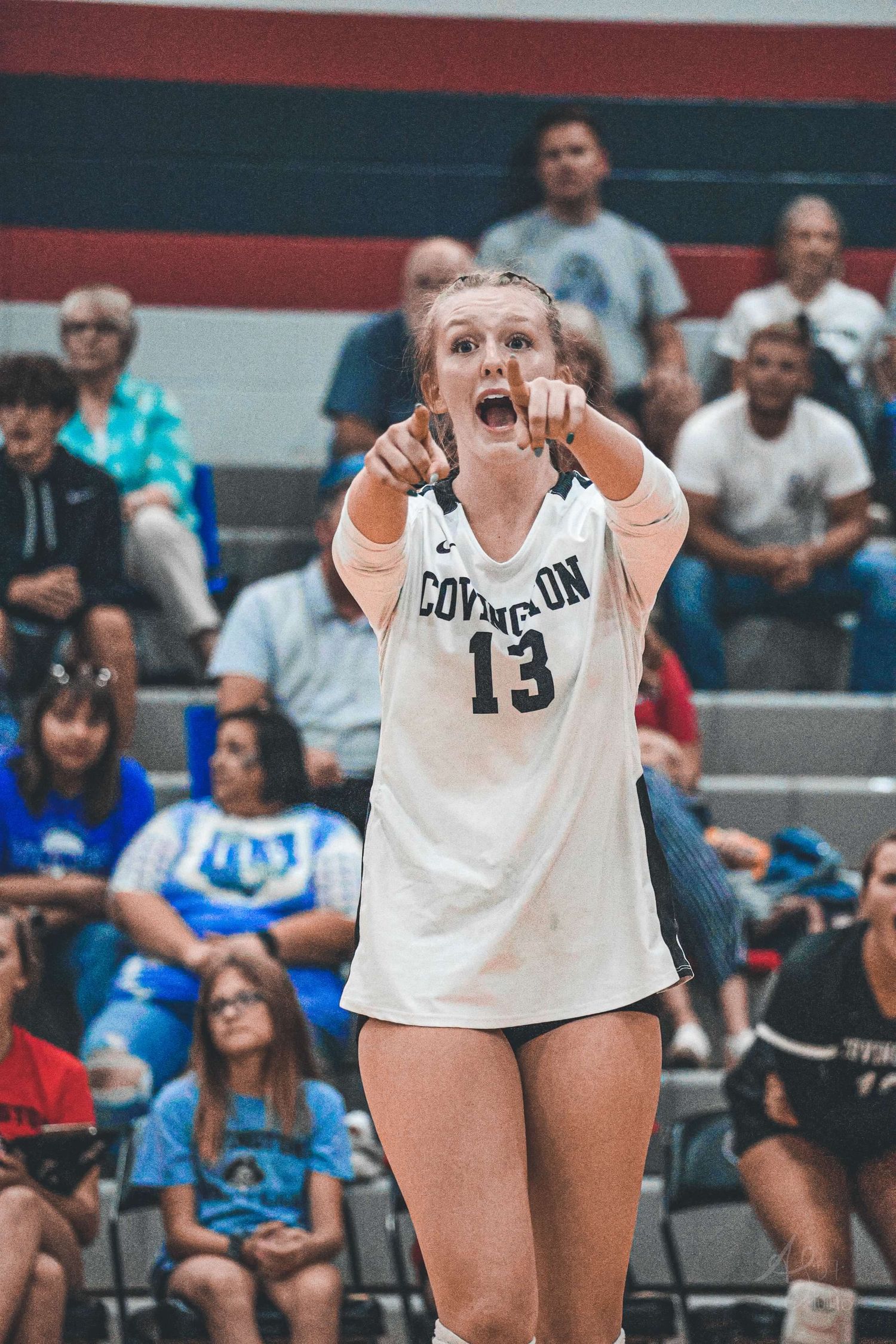 Female volleyball players in white uniforms prepare to receive a serve during an intense match.
