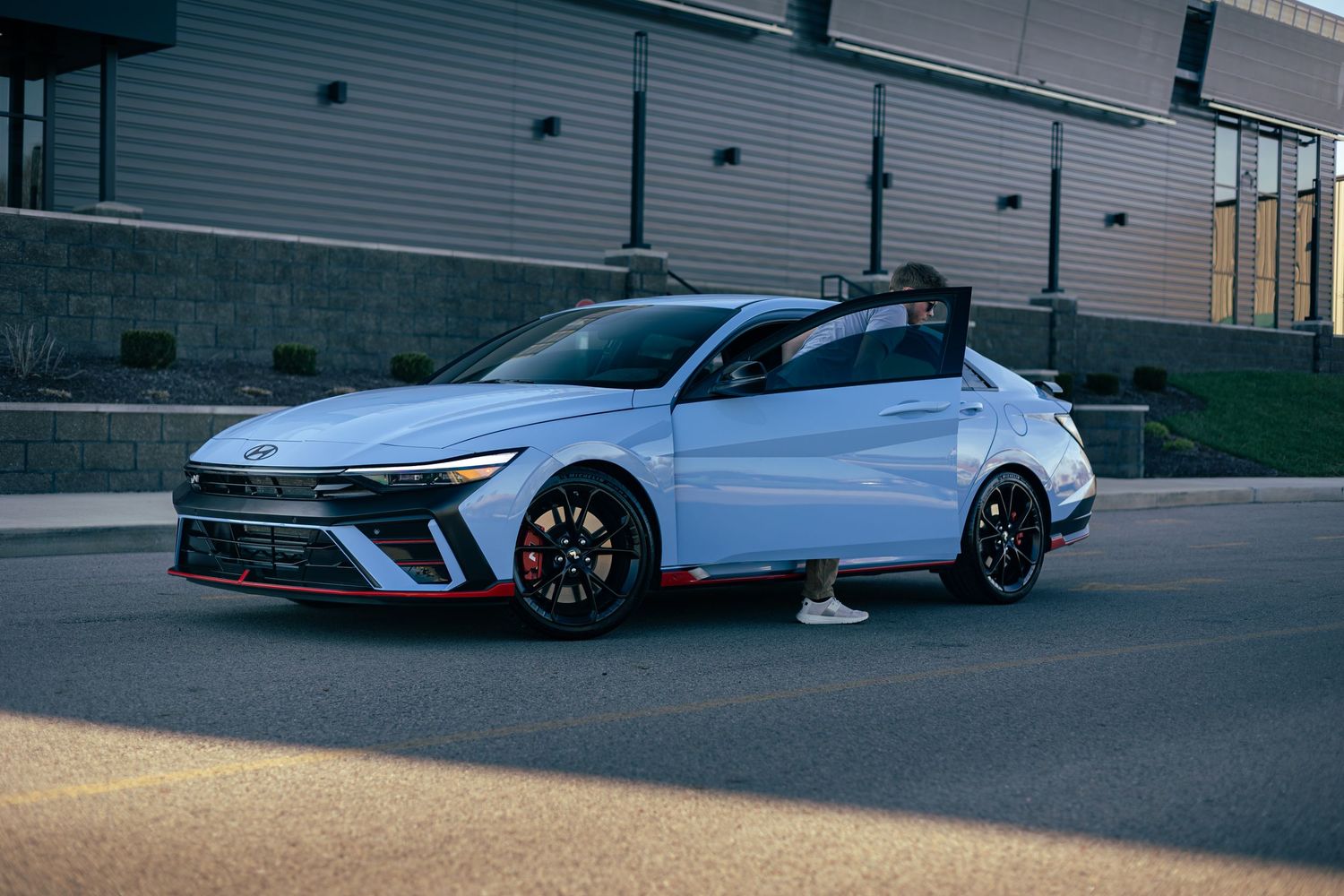 A white Hyundai Elantra N performance sedan with red accents and black wheels parked on a street at dusk.