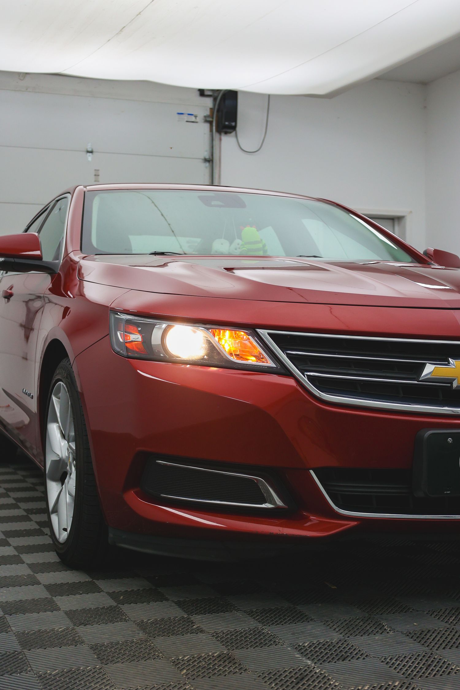 Front view of a red Chevrolet Impala sedan with illuminated headlights parked in a garage with checkered floor tiles.