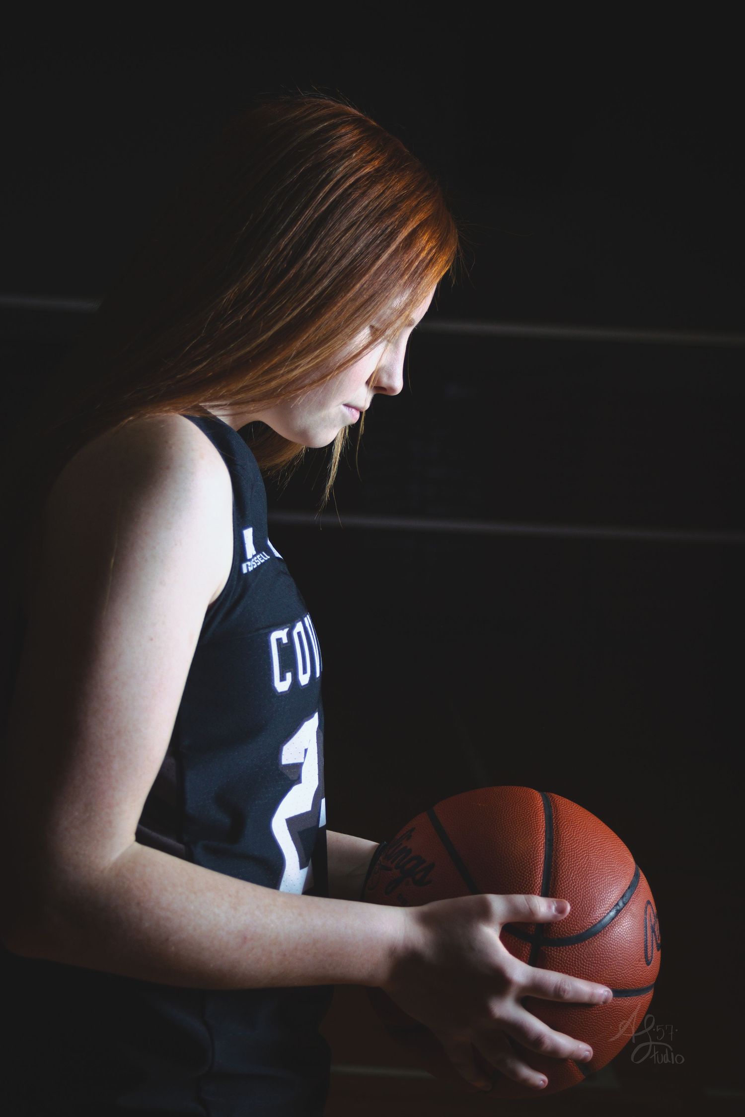 Basketball player in dark jersey holding ball in dramatic lighting.