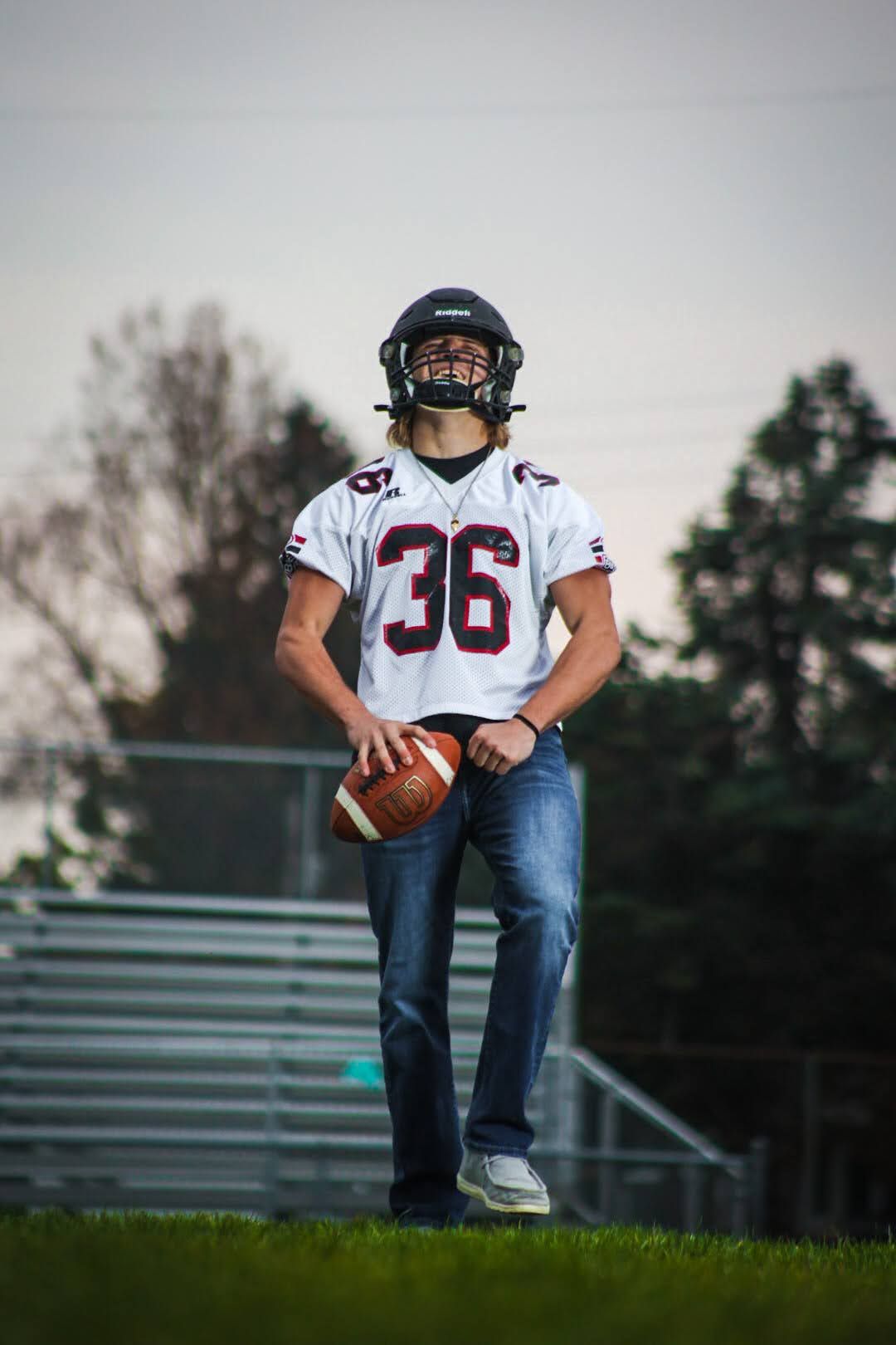Football player in white jersey number 36 posing with ball on field at dusk.