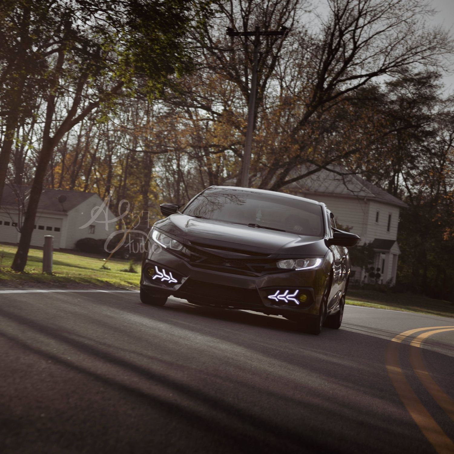 Low-angle shots of a dark sports car on a tree-lined street.