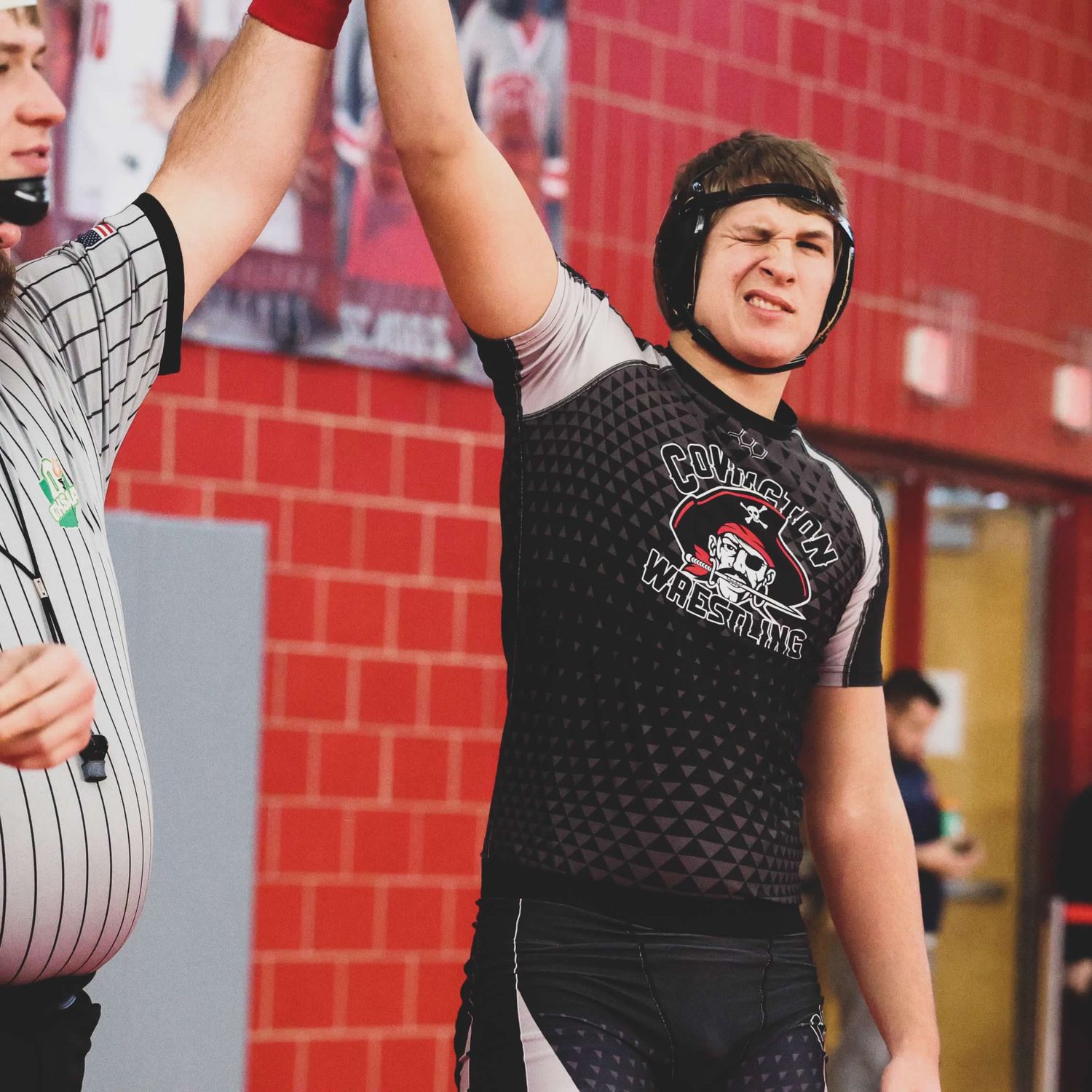 Wrestler celebrates victory with raised arm in front of red wall.