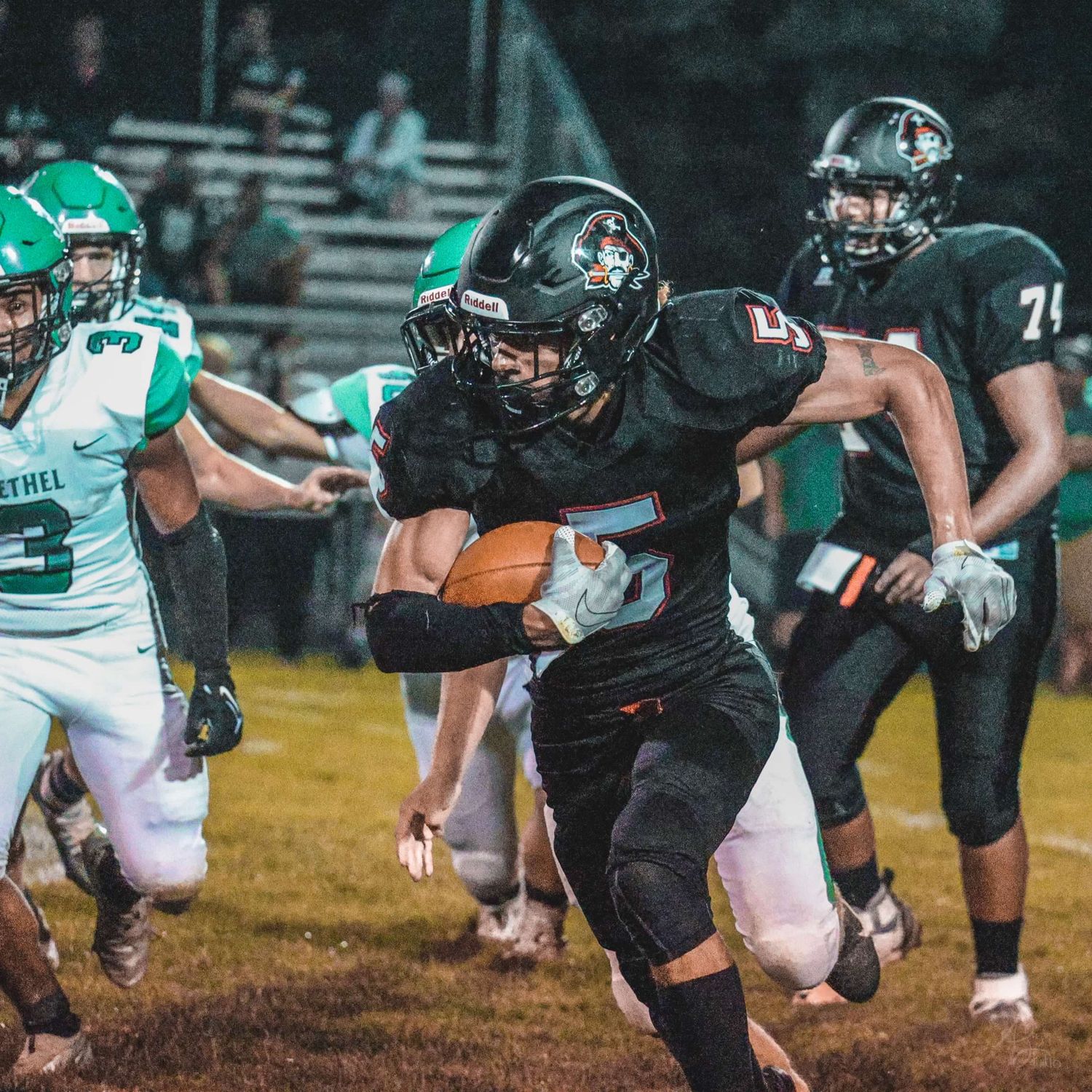 Football player in black uniform carries ball while evading defenders.
