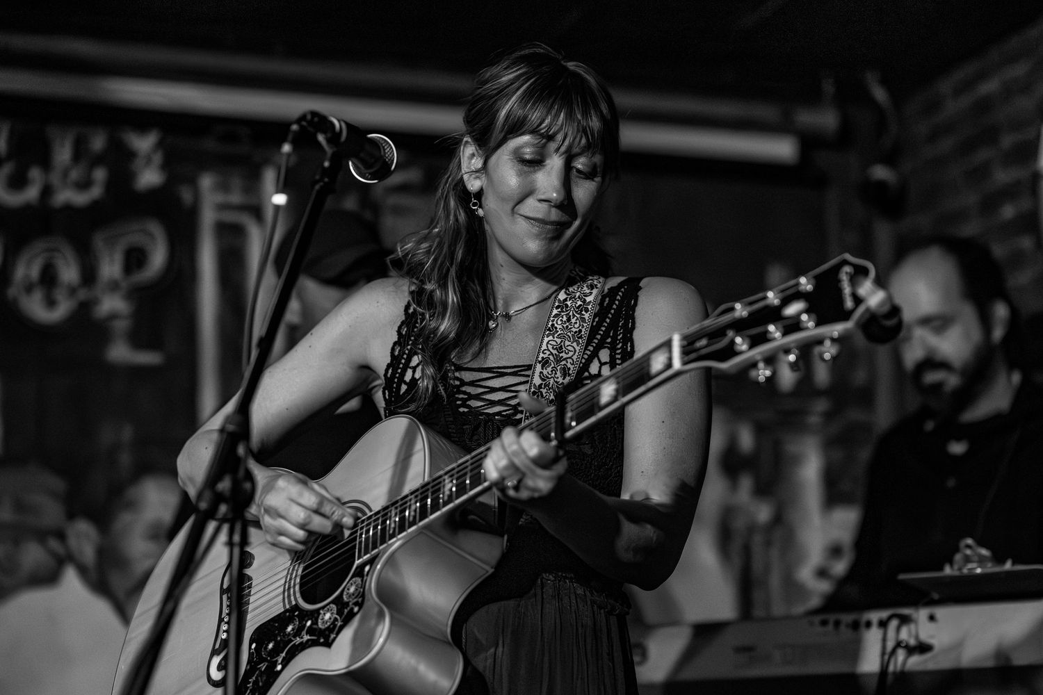 Woman playing acoustic guitar on stage in black and white live music performance photo.