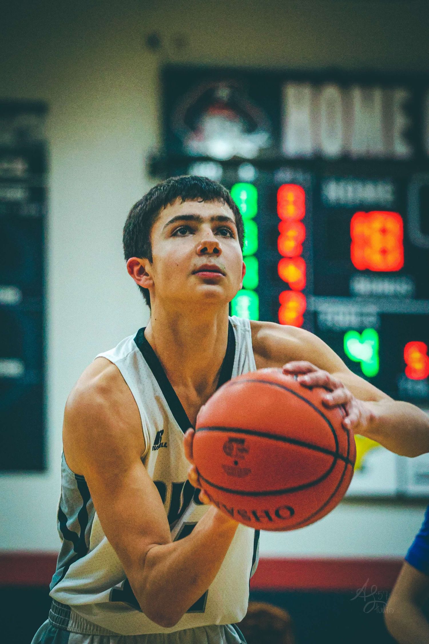 Basketball player takes aim at the hoop during a game with scoreboard visible in background.
