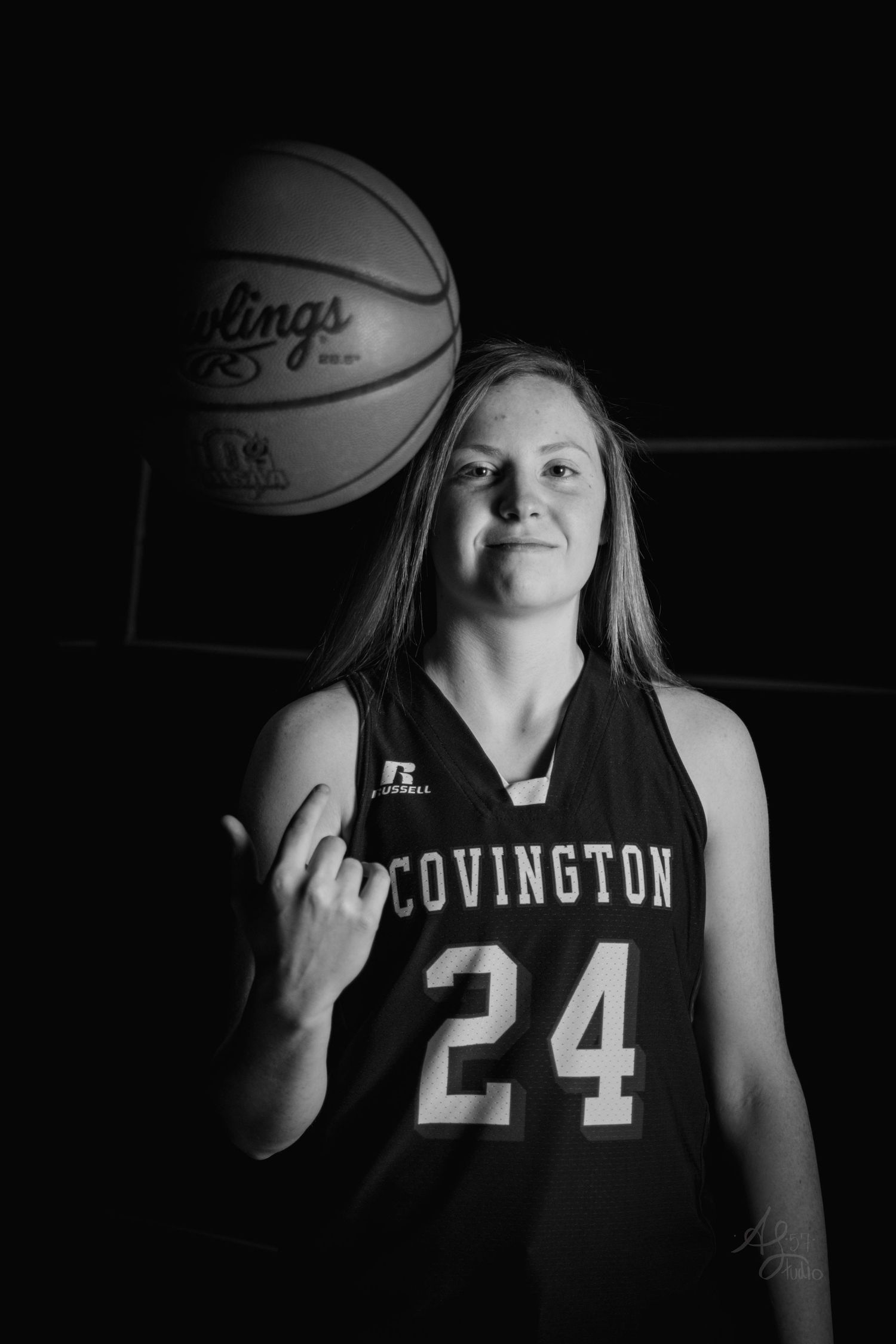 Basketball player in Covington jersey number 24 posing with ball in dramatic black and white portrait.