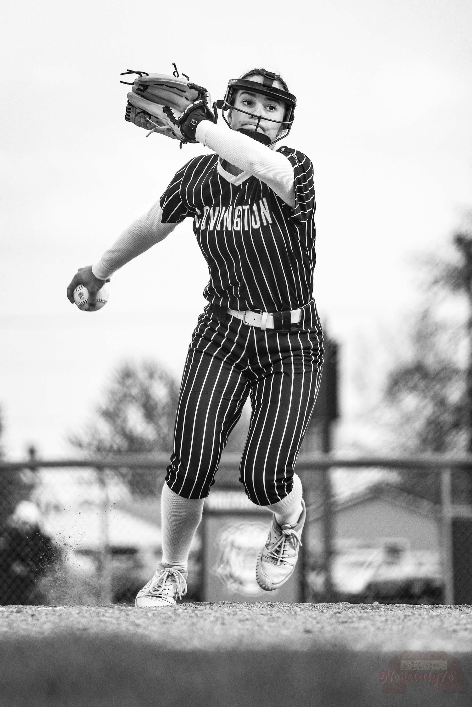 Softball pitcher in pinstriped uniform mid-throw during game.