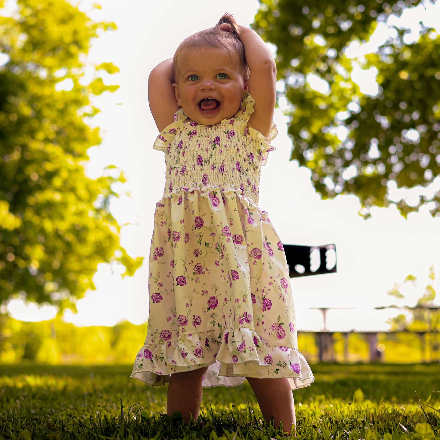 Baby in floral dress walking on grass during golden hour sunset.