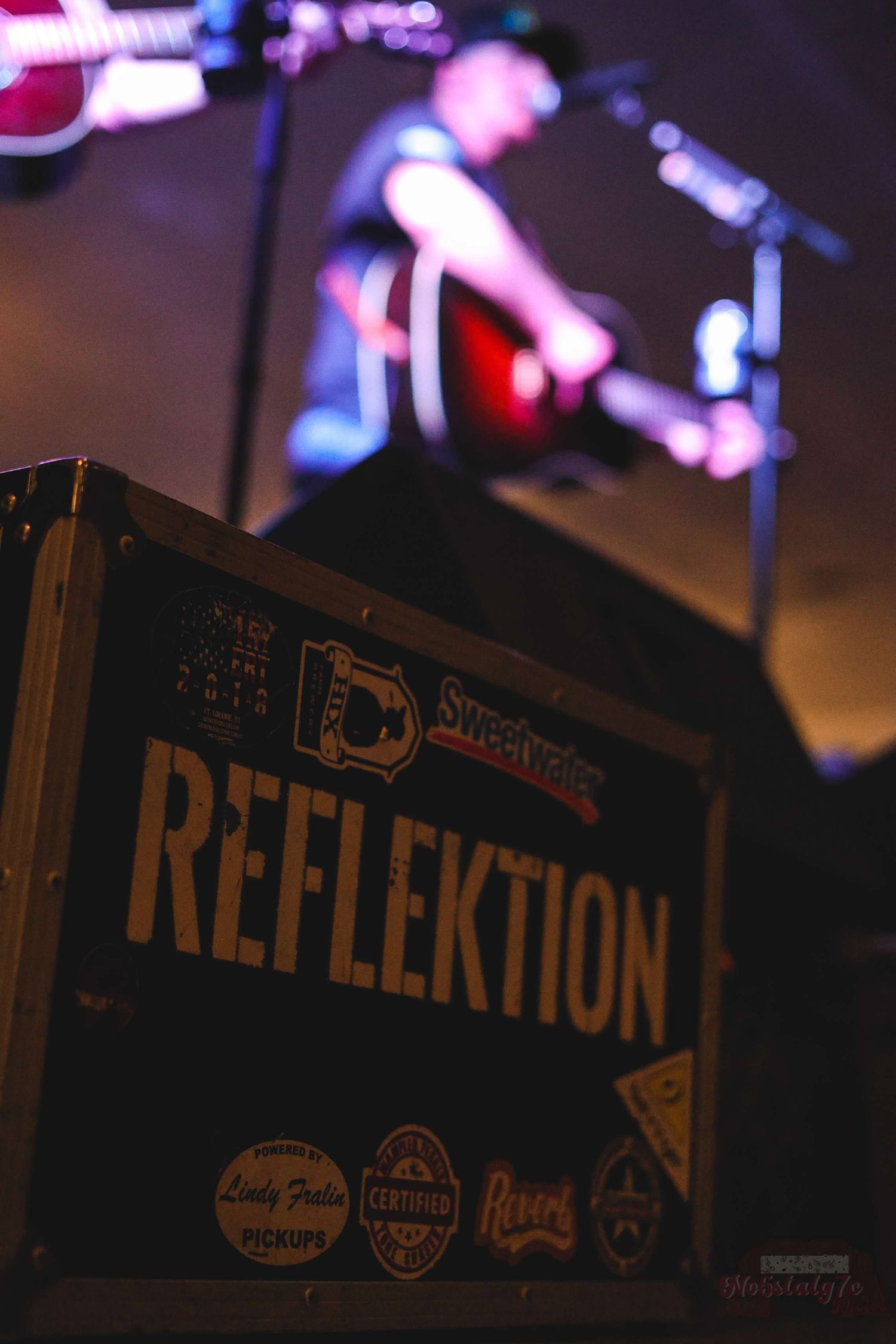 Reflection text displayed on dark signage with blurred stage lights in background.
