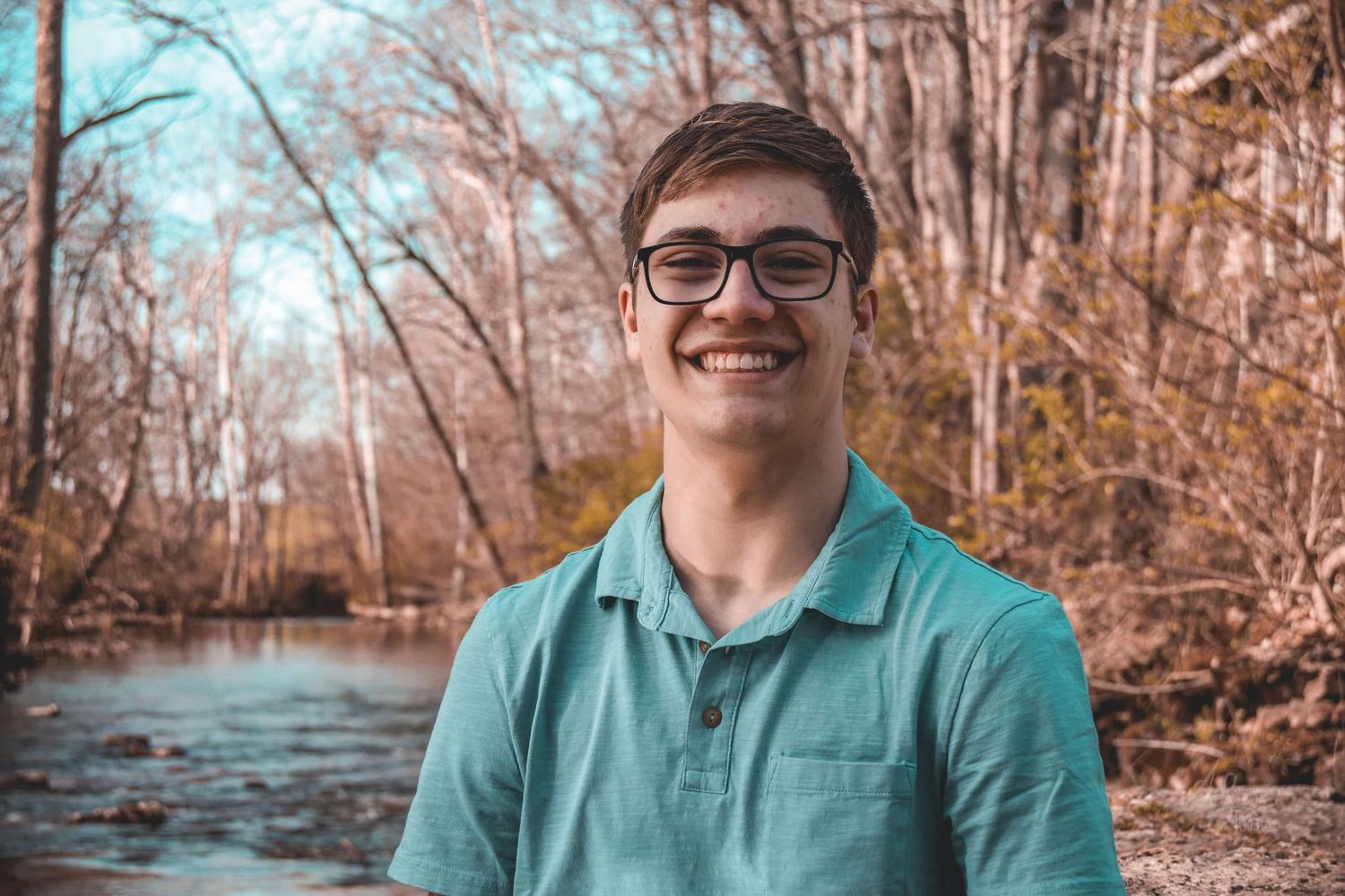 Portrait session in a wooded area with autumn trees and water in the background.