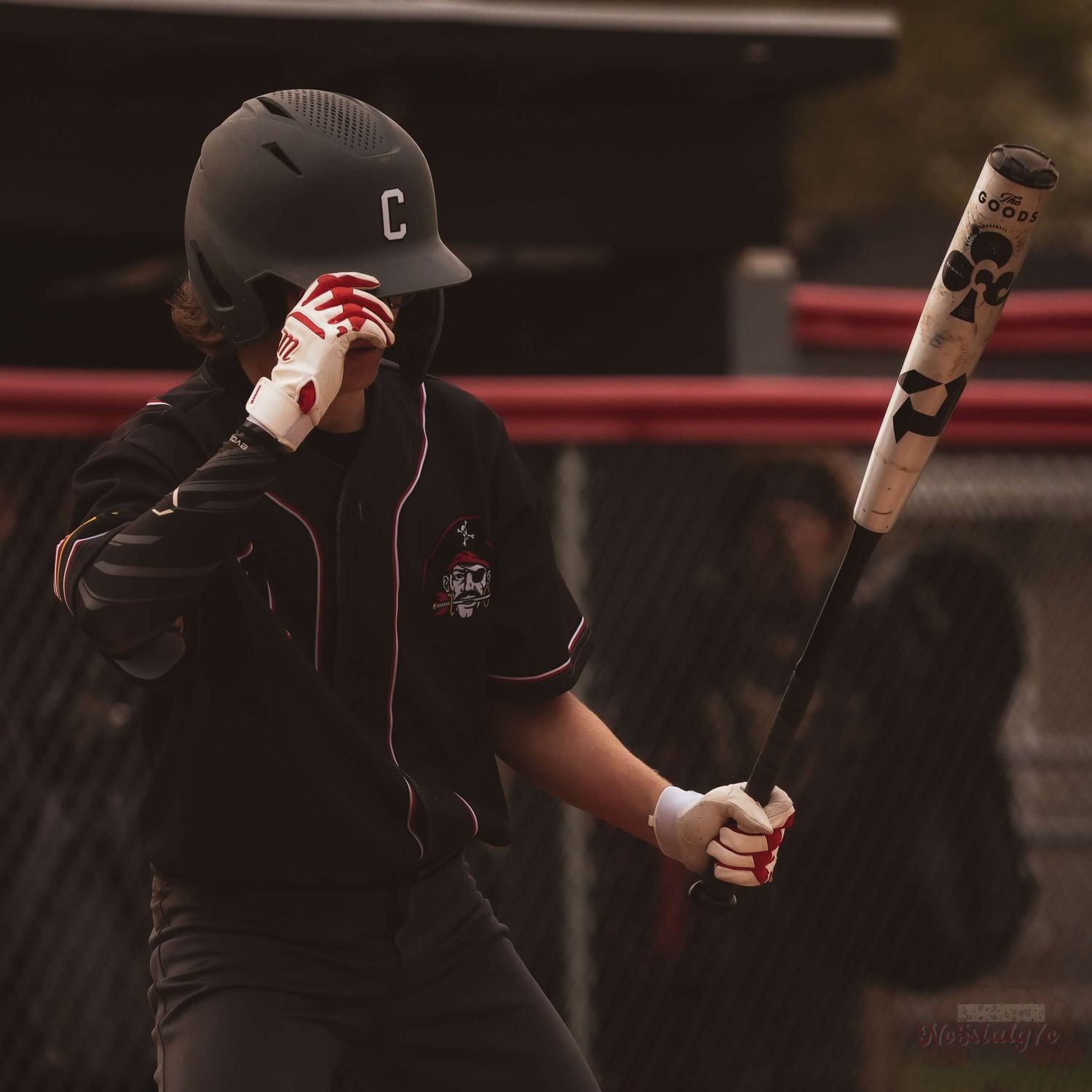 Baseball player in dark uniform adjusts helmet while holding bat.