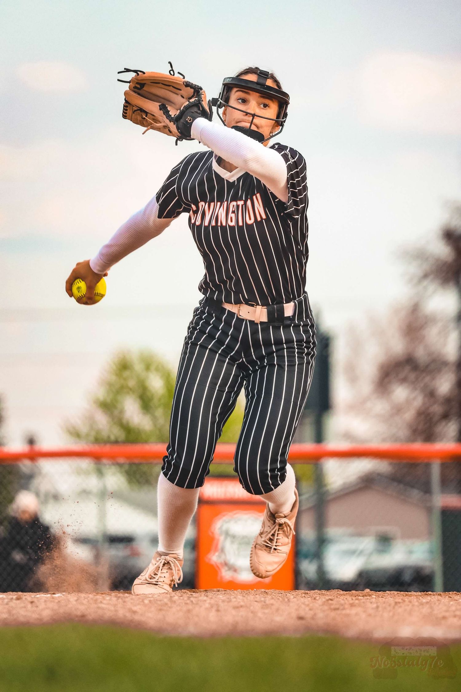 Softball pitcher in striped uniform winds up for pitch during game.