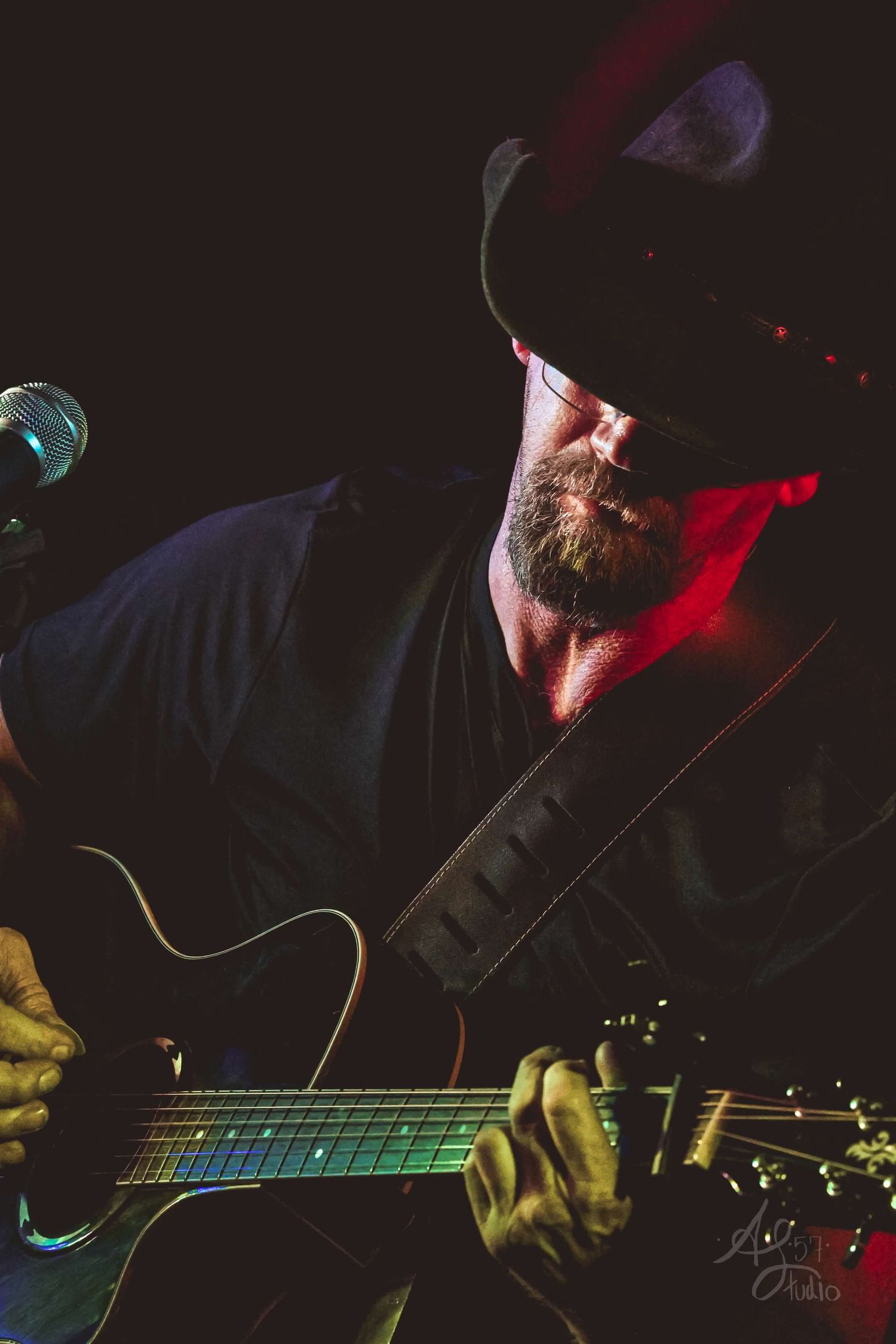 Close-up of hands playing electric guitar with dramatic red and blue stage lighting.