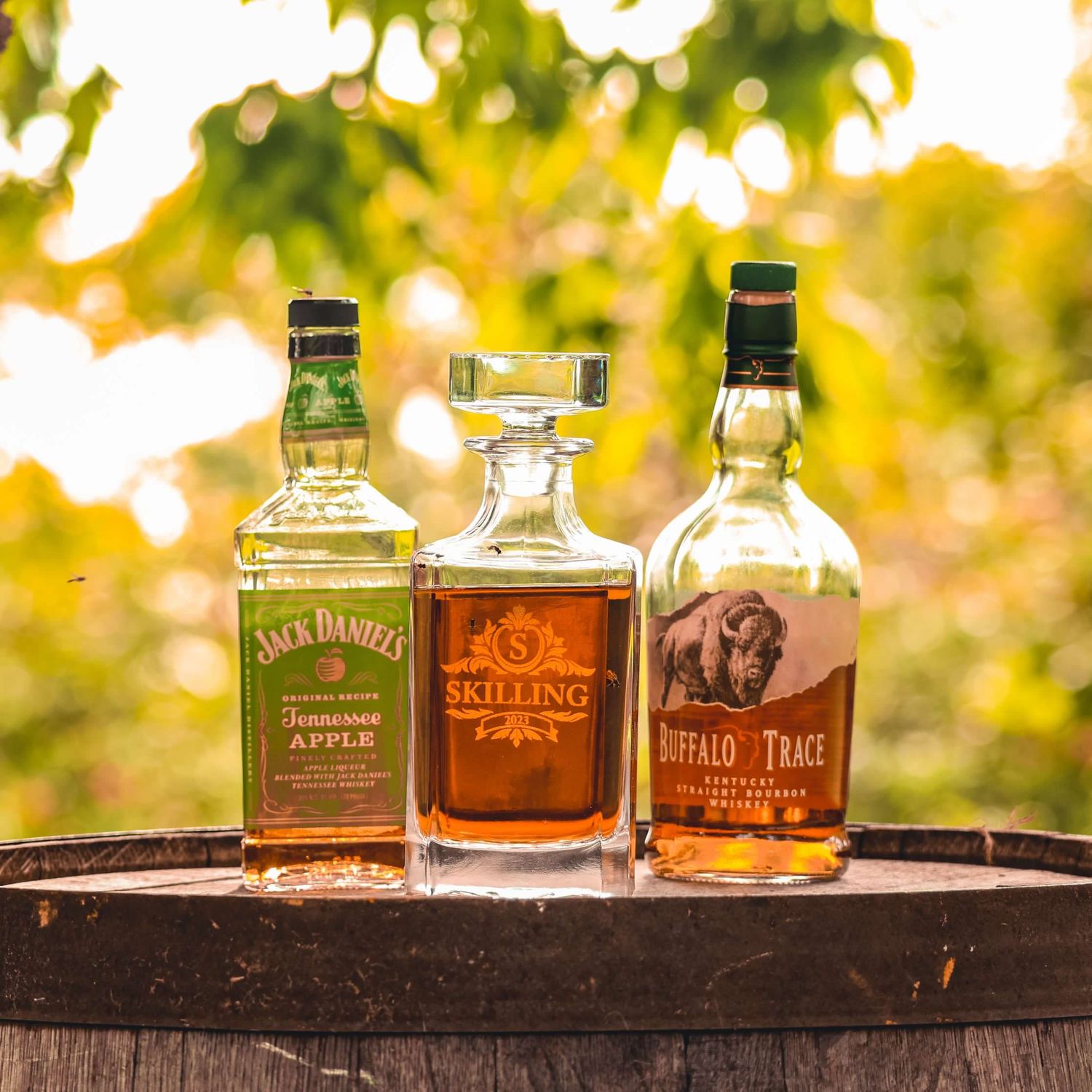 Collection of whiskey bottles lined up on rustic wooden surface with golden sunset backdrop.