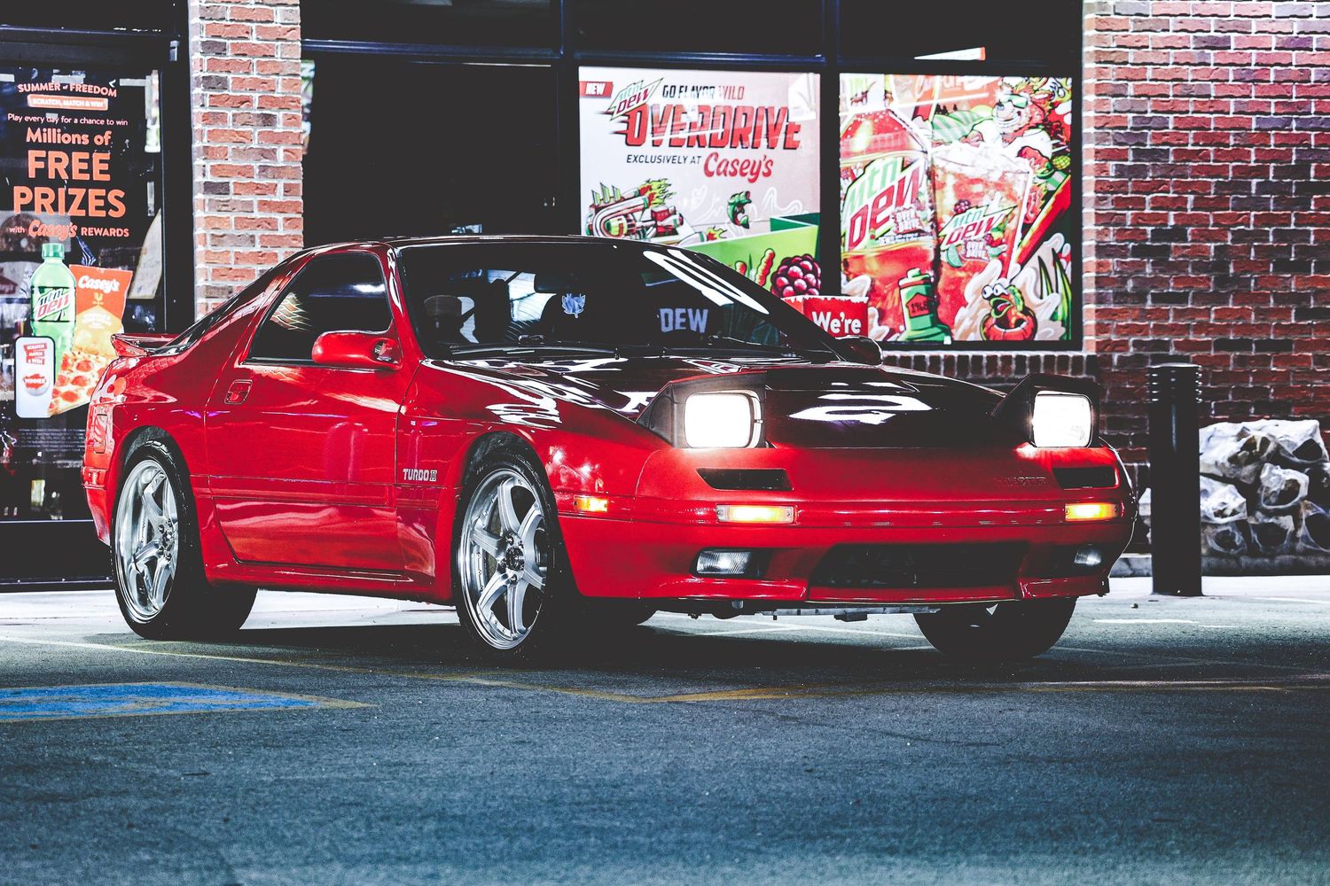Row of red sports cars parked in front of a brick building at night.